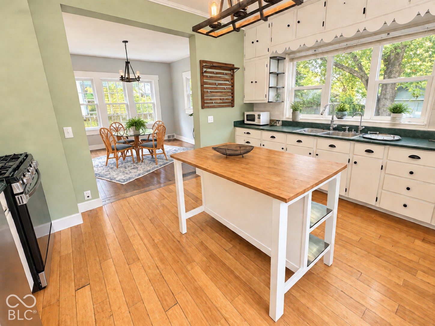 Kitchen featuring wood-finish flooring, white cabinetry with scalloped trim, wood-topped kitchen island, and metal pendant lighting