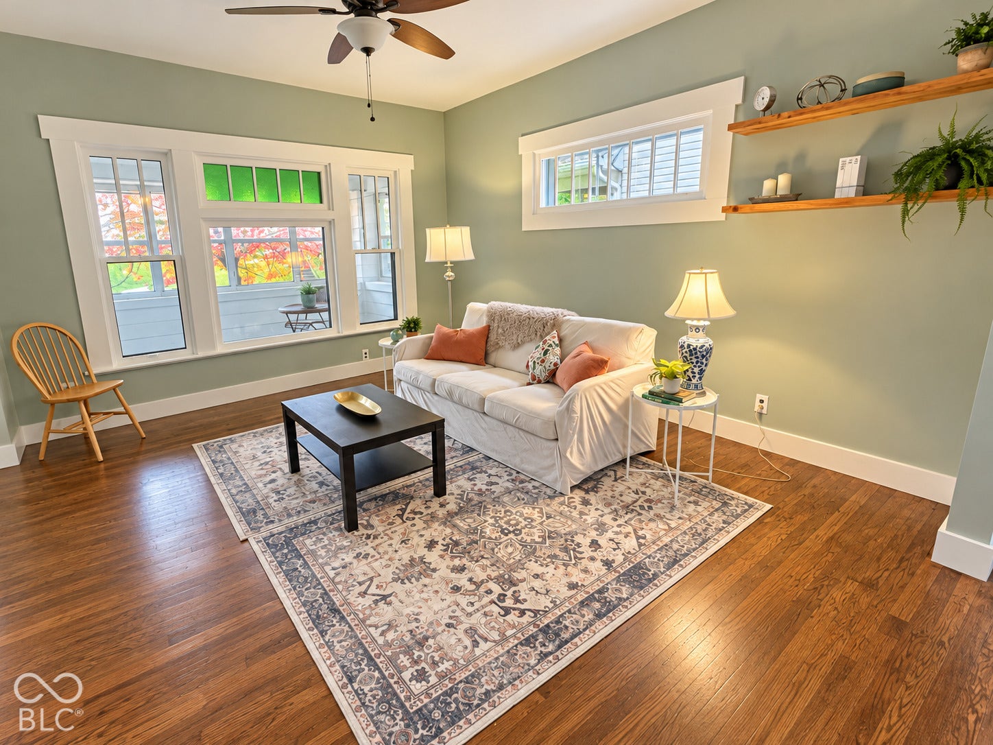 Hardwood flooring, multi-pane windows with decorative stained-glass transoms, built-in wooden shelving, and a ceiling fan