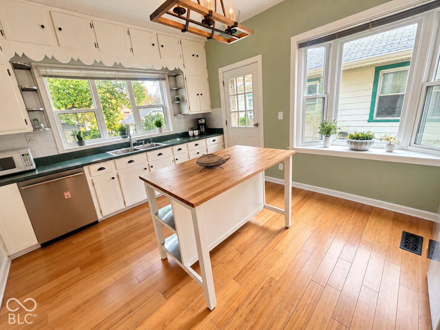 Kitchen featuring wood-finish flooring, white cabinetry with scalloped trim, a central kitchen island with a wood-surface countertop, and a box bay window
