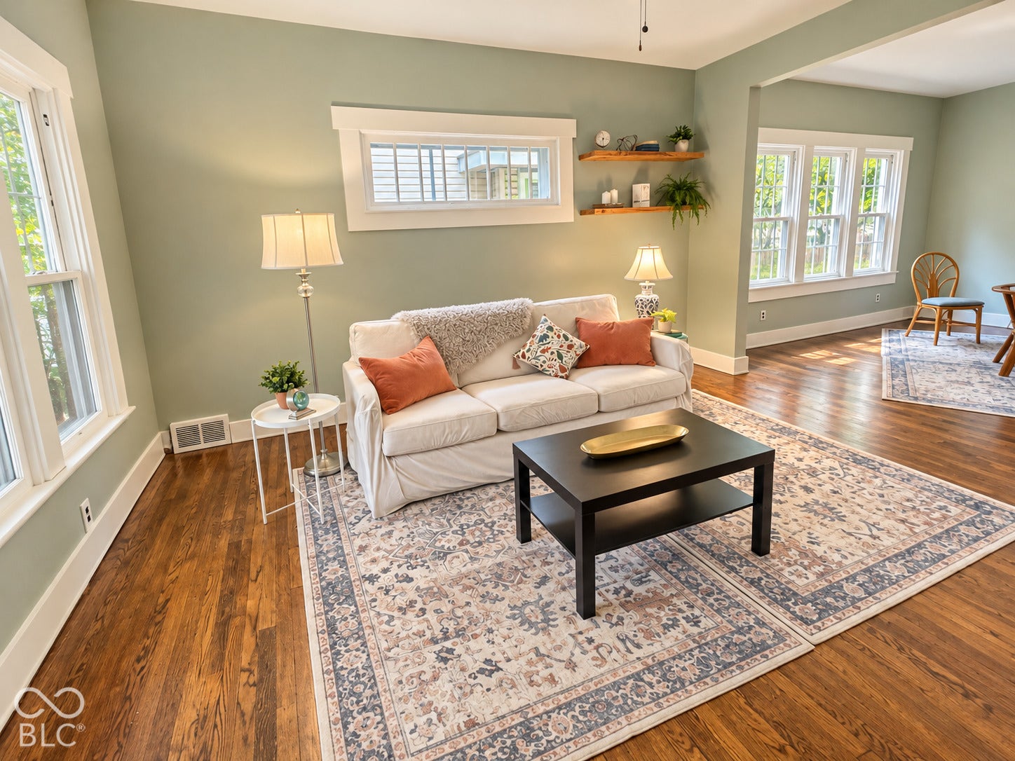 Living area featuring wood-finish flooring, multi-pane windows, a horizontal transom window, and wall-mounted natural wood shelving