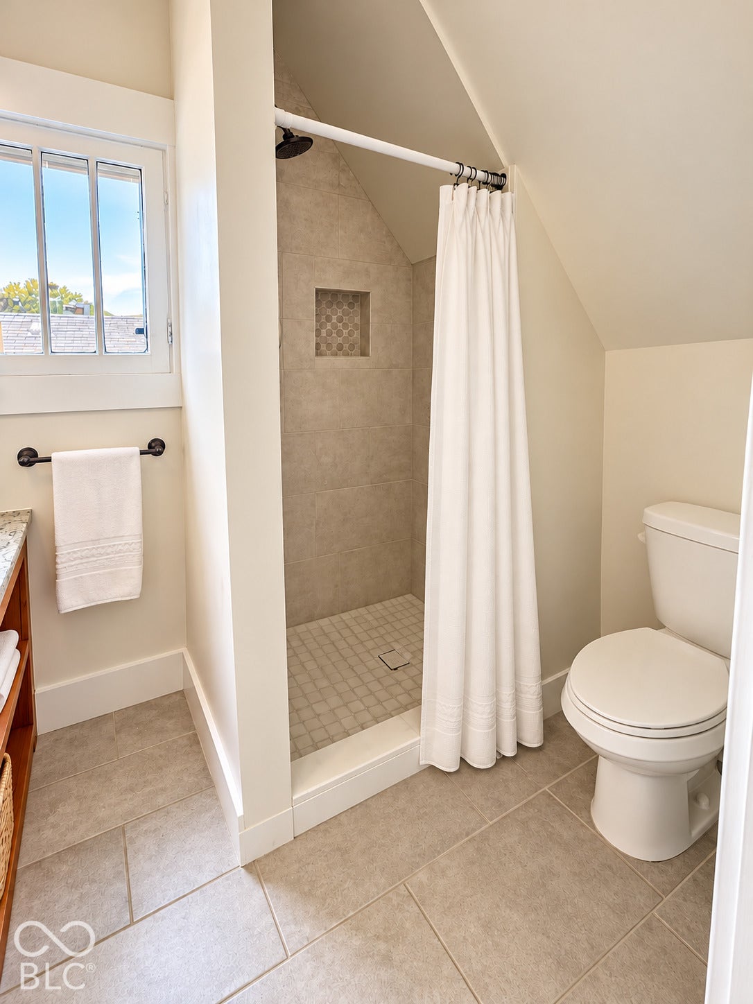 Virtually Altered - Bathroom featuring a tiled shower enclosure with a built-in recessed niche, stone-finish floor tiling, a multi-pane window, and a standard toilet