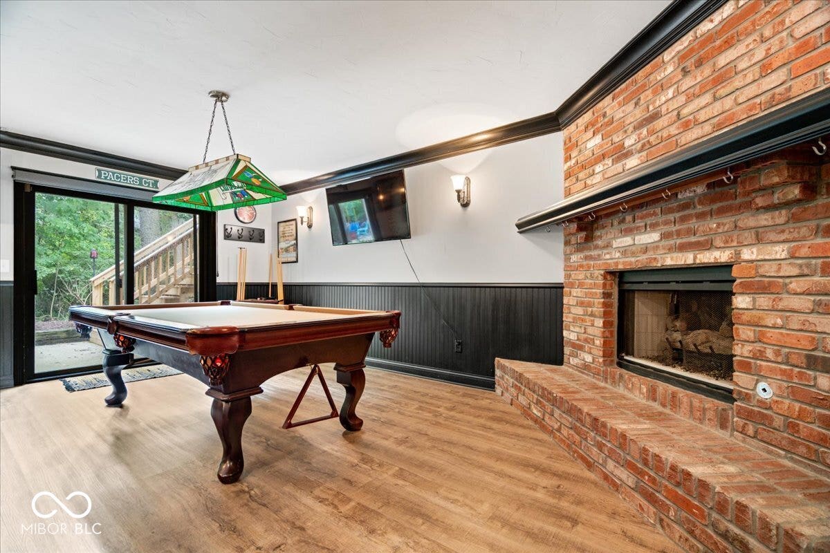 Floor-to-ceiling brick fireplace with a raised masonry hearth, wood-finish flooring, beadboard wainscoting, and sliding glass doors with exterior egress