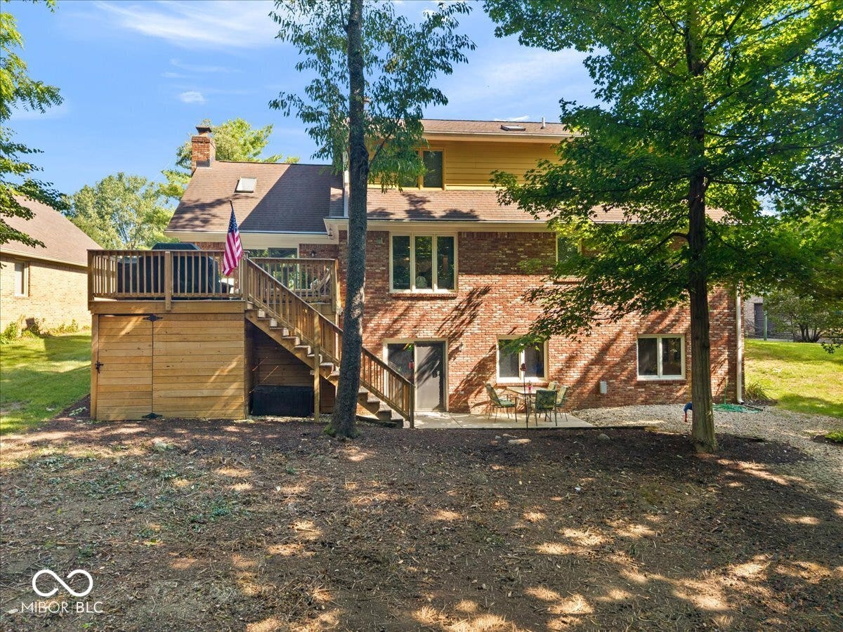 Brick exterior featuring a wood-tone deck with railing, exterior staircase, and patio area