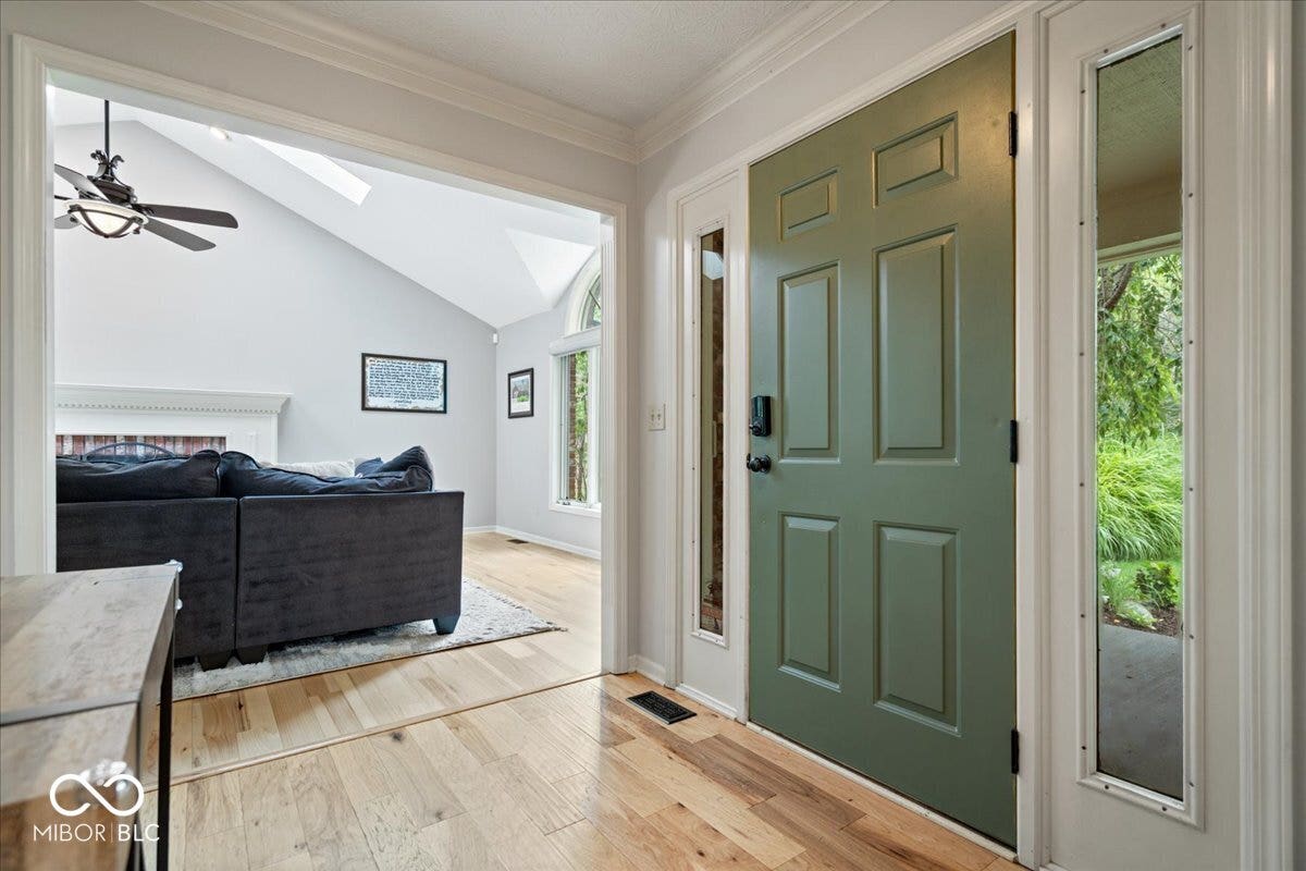 Entryway featuring wood-finish flooring, a paneled door with dual sidelights, crown molding, and vaulted ceilings