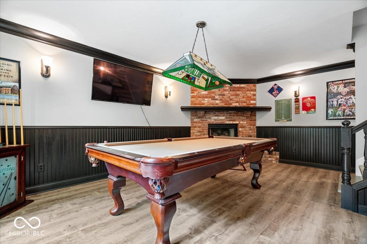 Exposed brick fireplace with a wood mantel, black wainscoting, wood-finish flooring, and wall-mounted sconce lighting