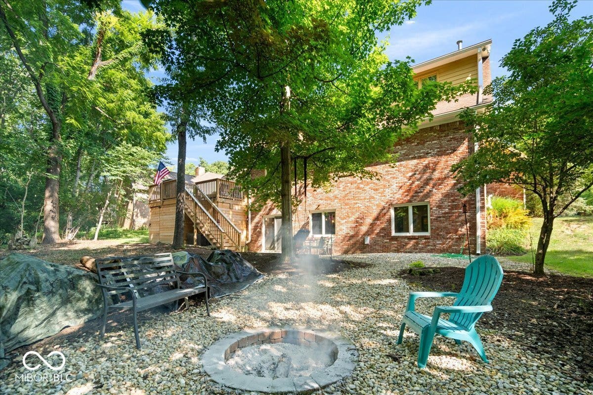 Terraced backyard featuring a stone fire pit, gravel ground cover, and mature trees
