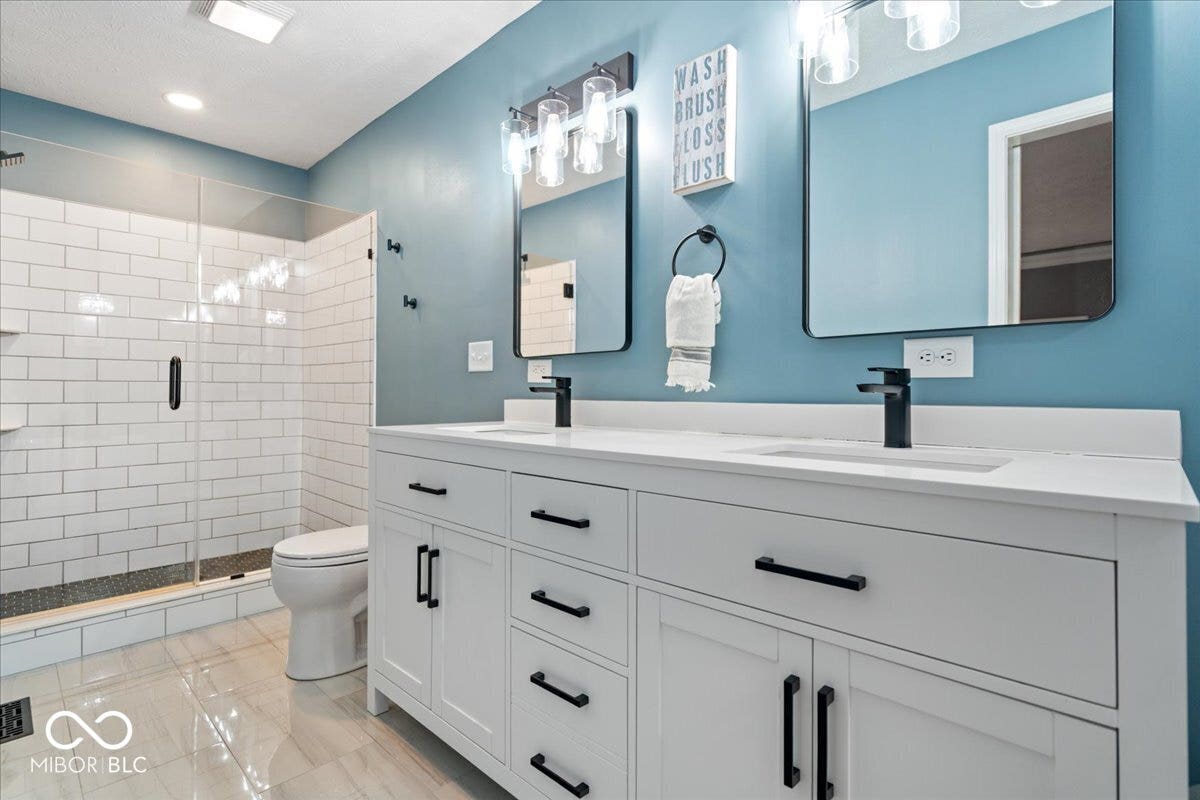 Double vanity with white cabinetry, rectangular vessel sinks, quartz countertops, and matte black hardware, paired with a glass-enclosed shower featuring white subway tile surround