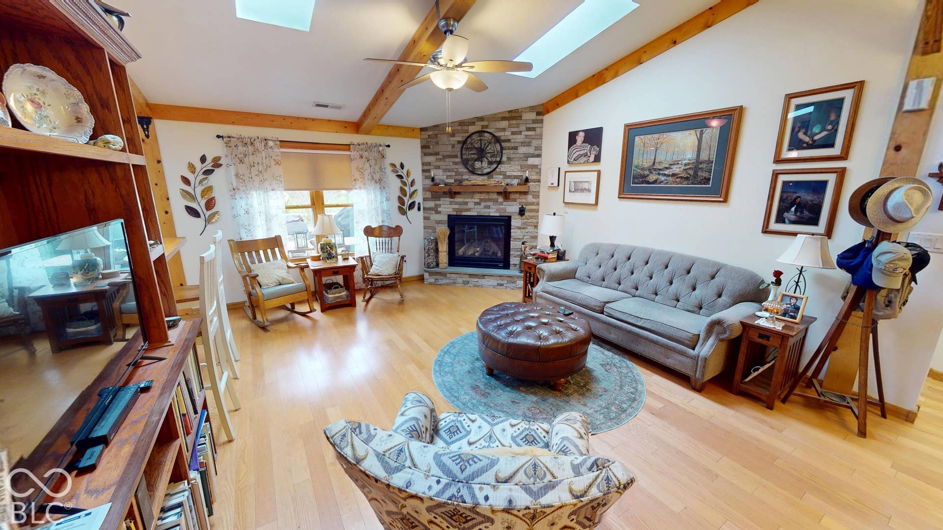 Vaulted ceiling with skylights, exposed wood beams, wood-finish flooring, and a stone-faced fireplace