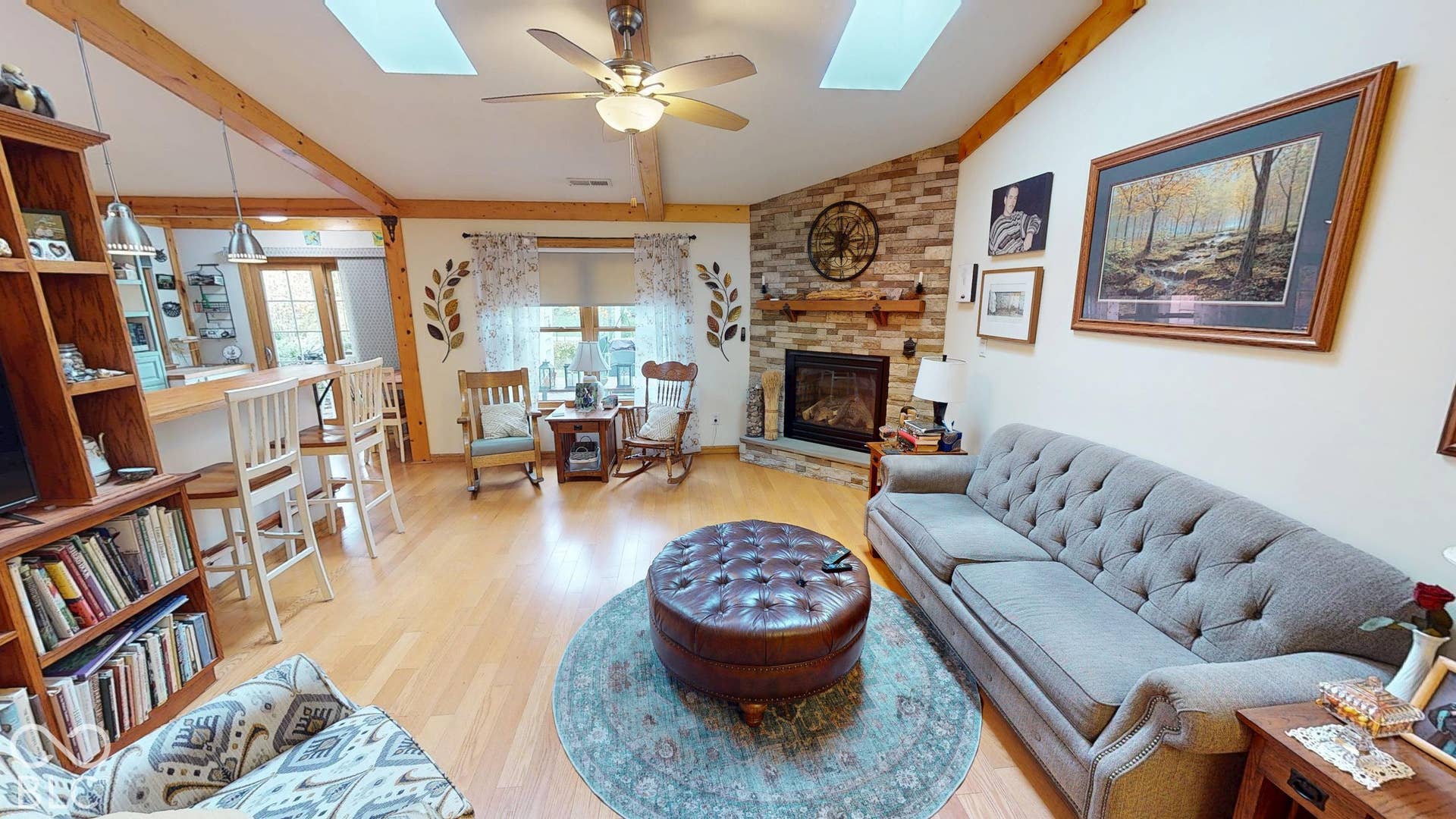 Vaulted ceiling with exposed wood beams, skylights, wood-finish flooring, and a stone-faced fireplace
