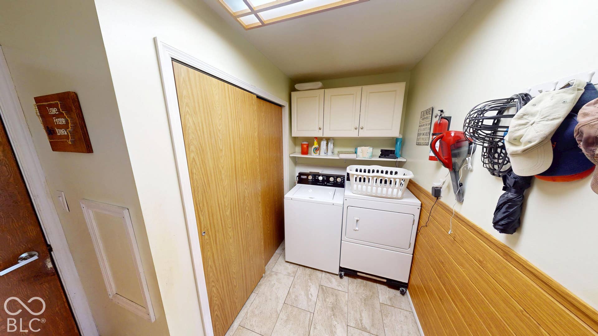 Laundry area with light-toned wall paneling, tile flooring, and white cabinetry