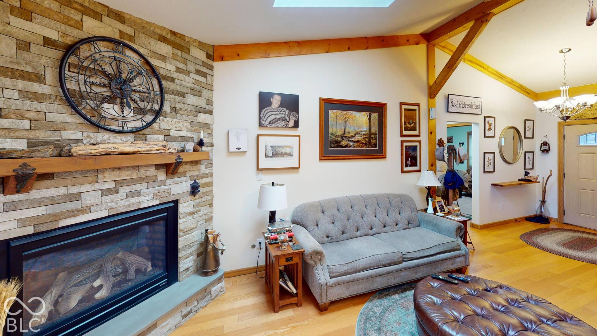 Stone-clad fireplace with a wood mantel, exposed wood beams, and light wood-finish flooring