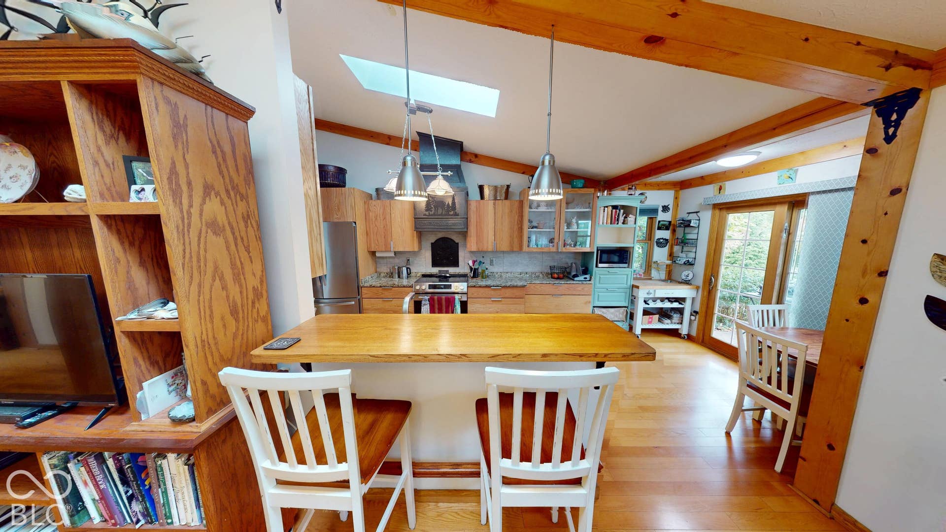 Vaulted ceiling with exposed beams, wood-finish flooring, kitchen with built-in cabinetry, breakfast bar, and skylight