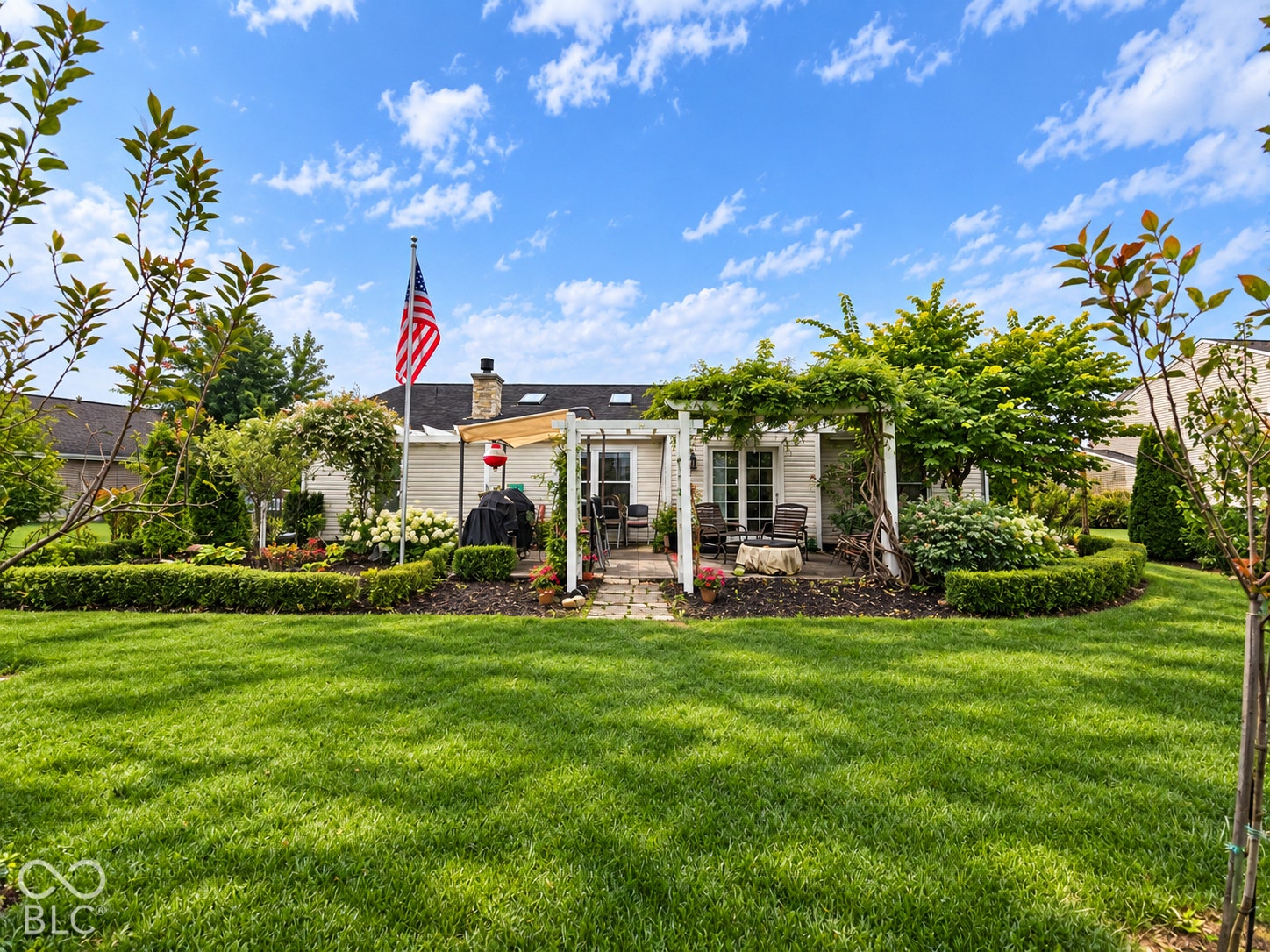 Expansive backyard featuring a manicured lawn, established landscaping, a brick paver patio, and a white pergola