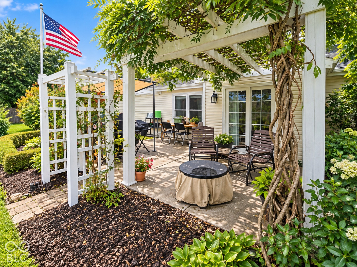 Patio area featuring a white pergola with mature vines, direct access through French doors, a paver pathway, and defined garden beds