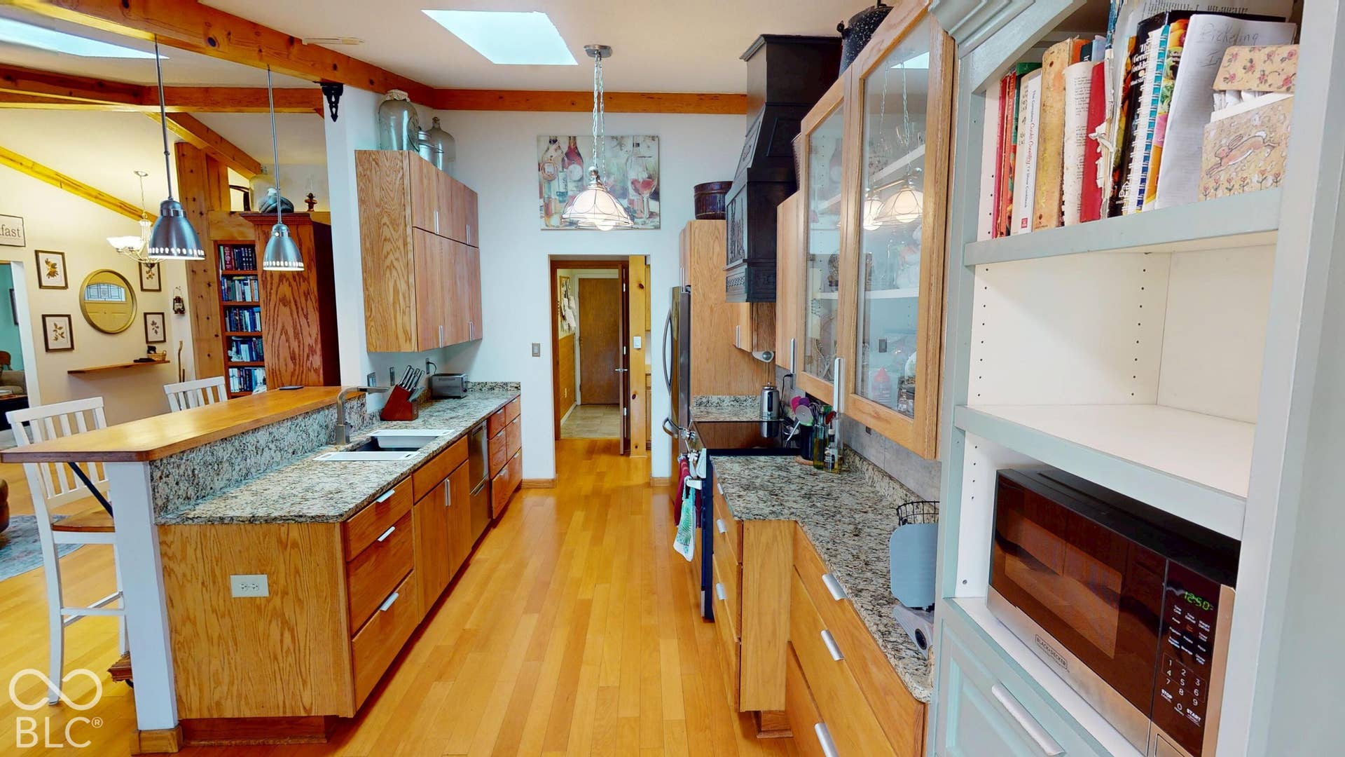 Galley kitchen with wood-finish flooring, granite countertops, wood-finish cabinetry, and a skylight