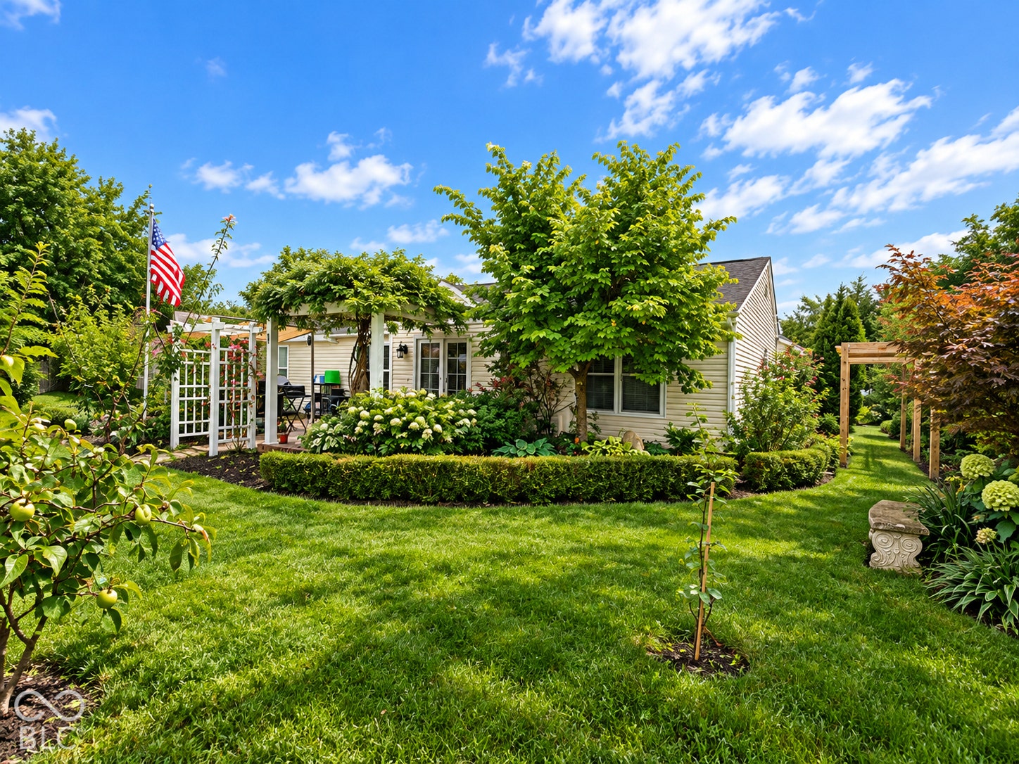 Expansive backyard featuring a lush lawn, established garden beds, white lattice arbor, and an additional wood arbor