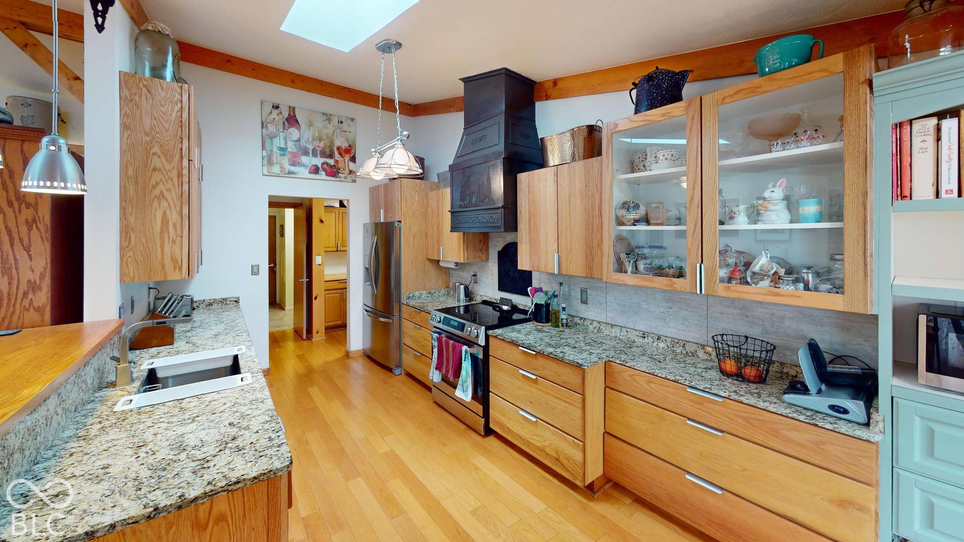 Wood-finish flooring, granite countertops, stainless steel appliances, exposed wood ceiling beams, and a skylight
