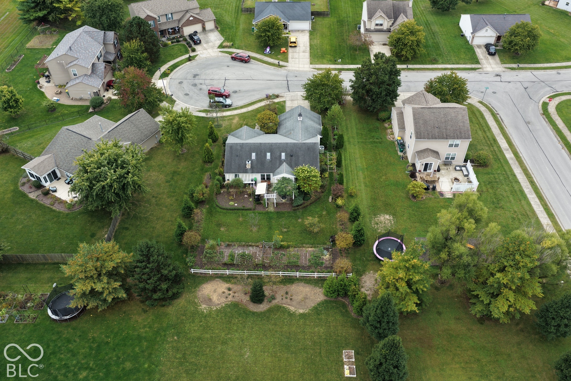 Aerial perspective of a residential property featuring a sprawling rear lawn, landscaped garden beds, perimeter fencing, and mature trees