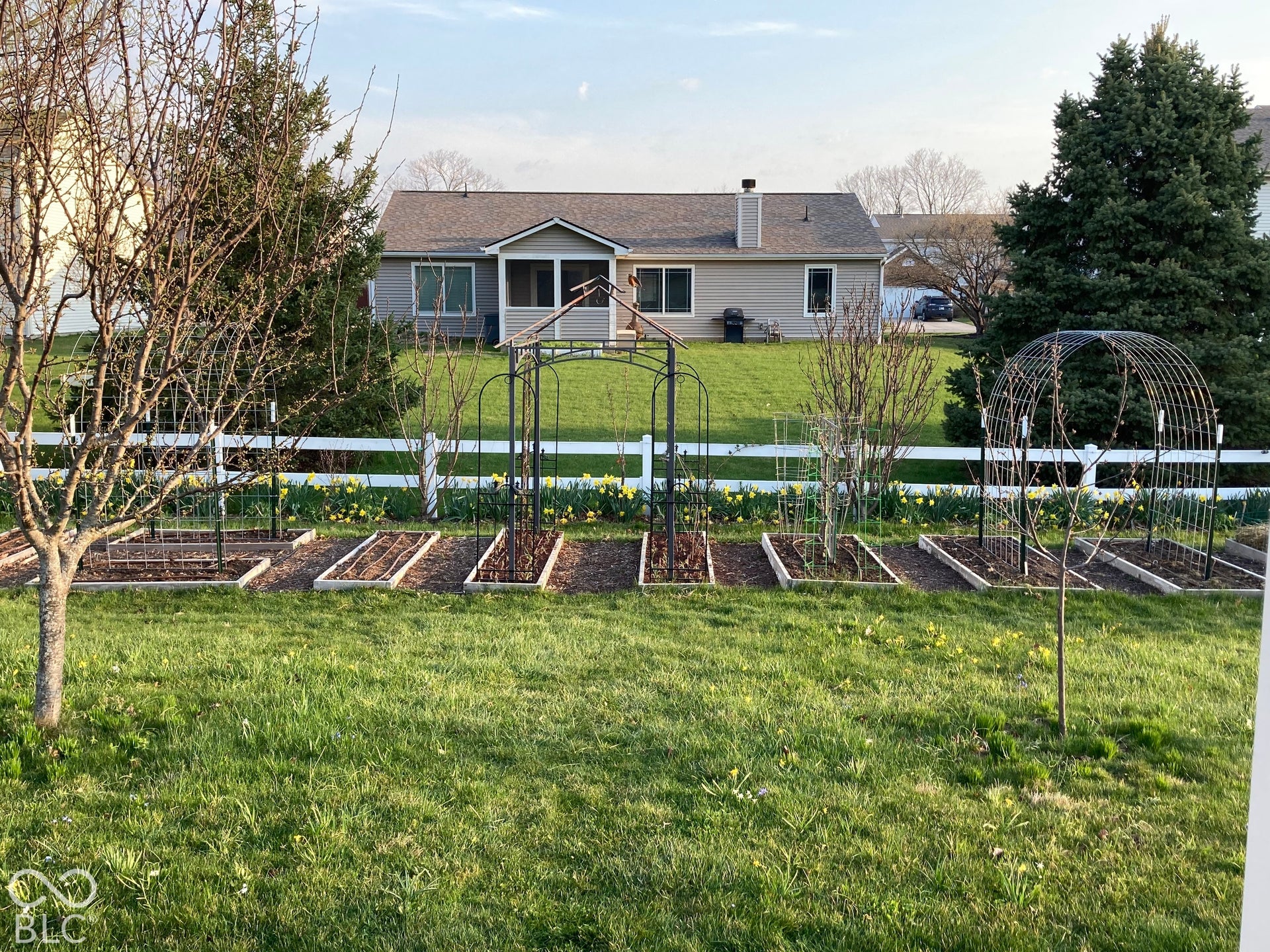 Backyard featuring raised garden beds, metal garden trellises, a white vinyl fence, and a screened-in porch