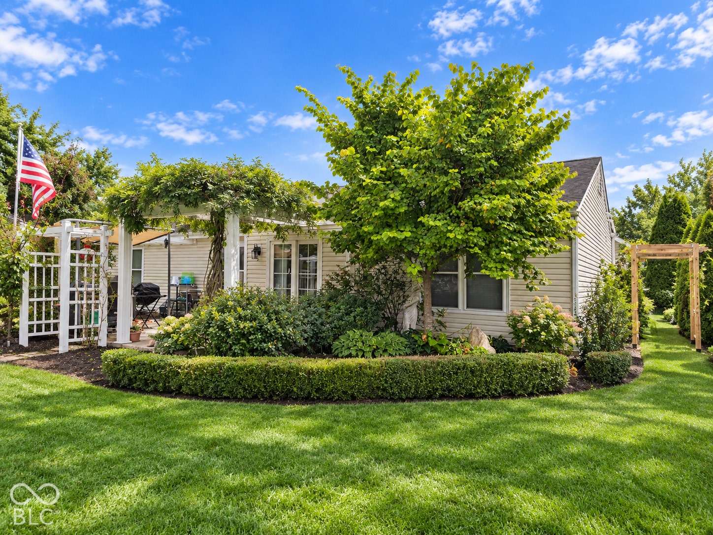 Manicured lawn with established landscaping, featuring a white pergola, covered patio area, and a secondary wooden pergola