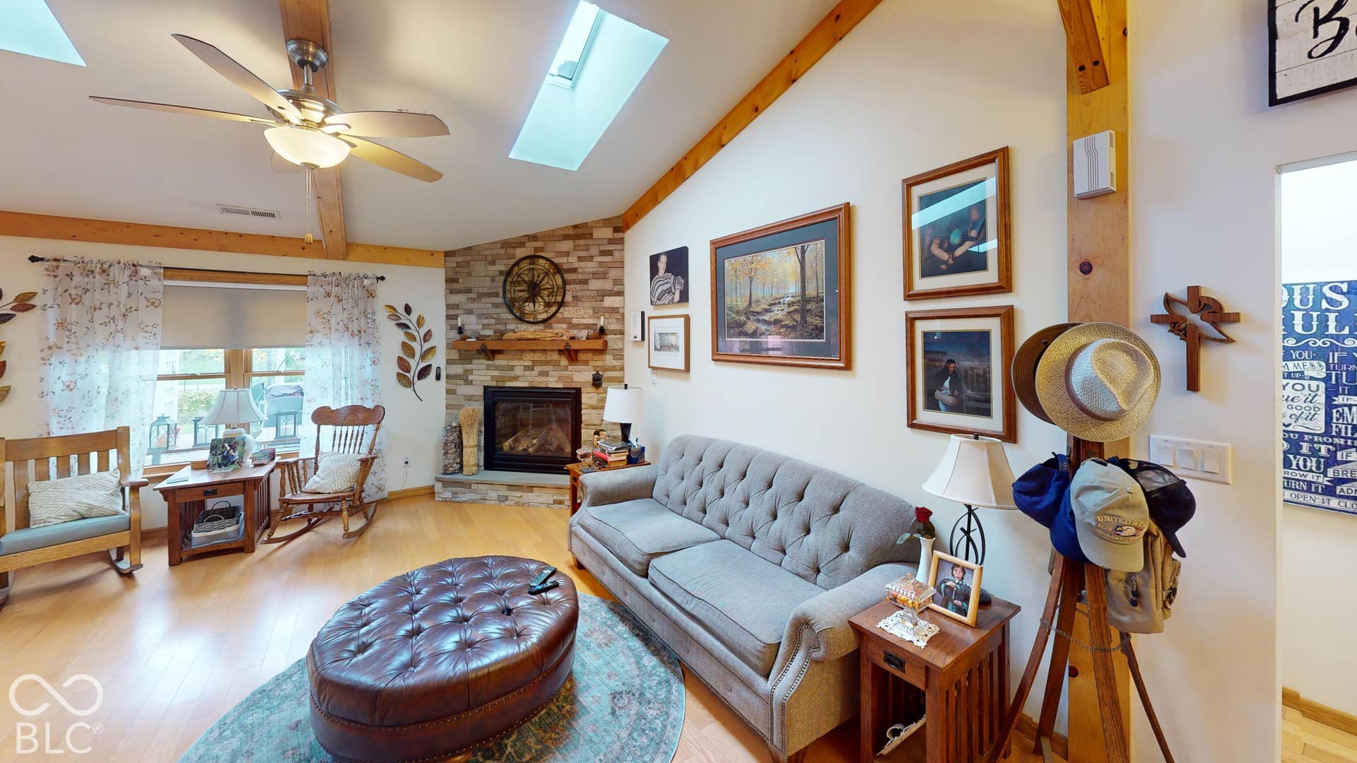 Vaulted ceiling with exposed wood beams, skylights, wood-finish flooring, and a stone-surround fireplace with a wood mantle