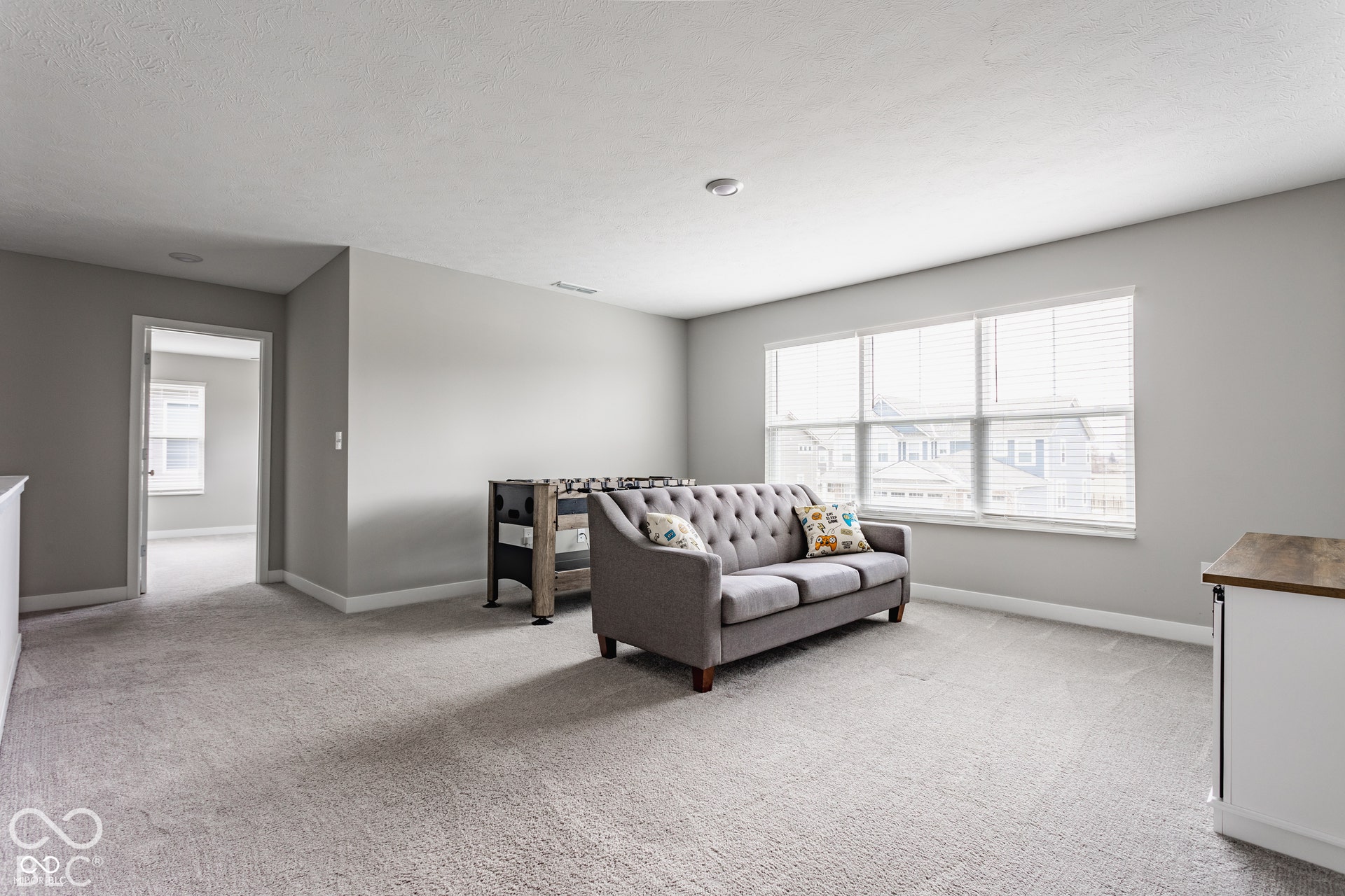Neutral-toned interior space featuring light-toned carpeting, recessed ceiling lighting, and a multi-pane window with integrated blinds