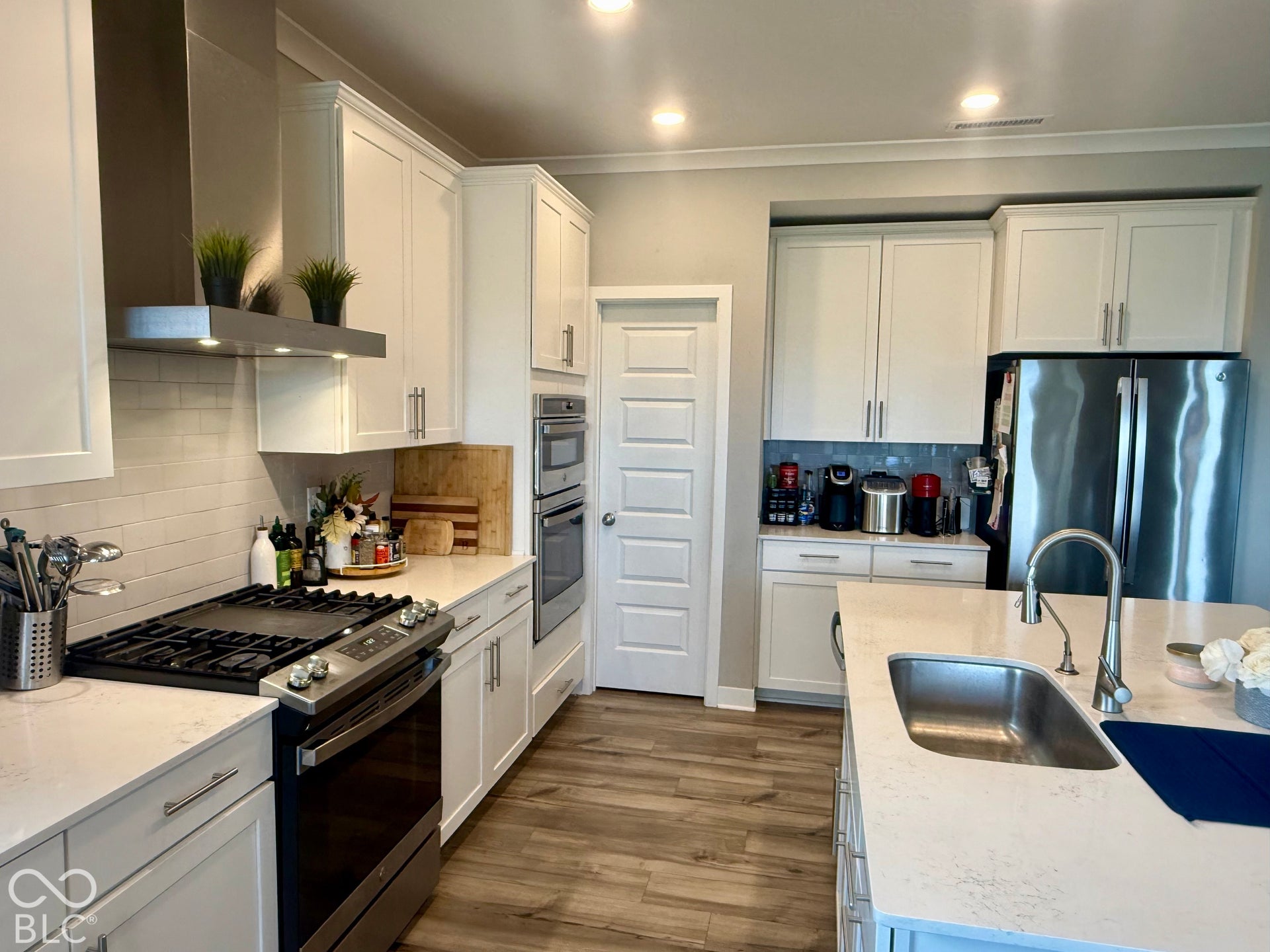 Kitchen featuring white cabinetry, quartz countertops, a central island with an undermount sink, built-in double wall ovens, and stainless steel appliances