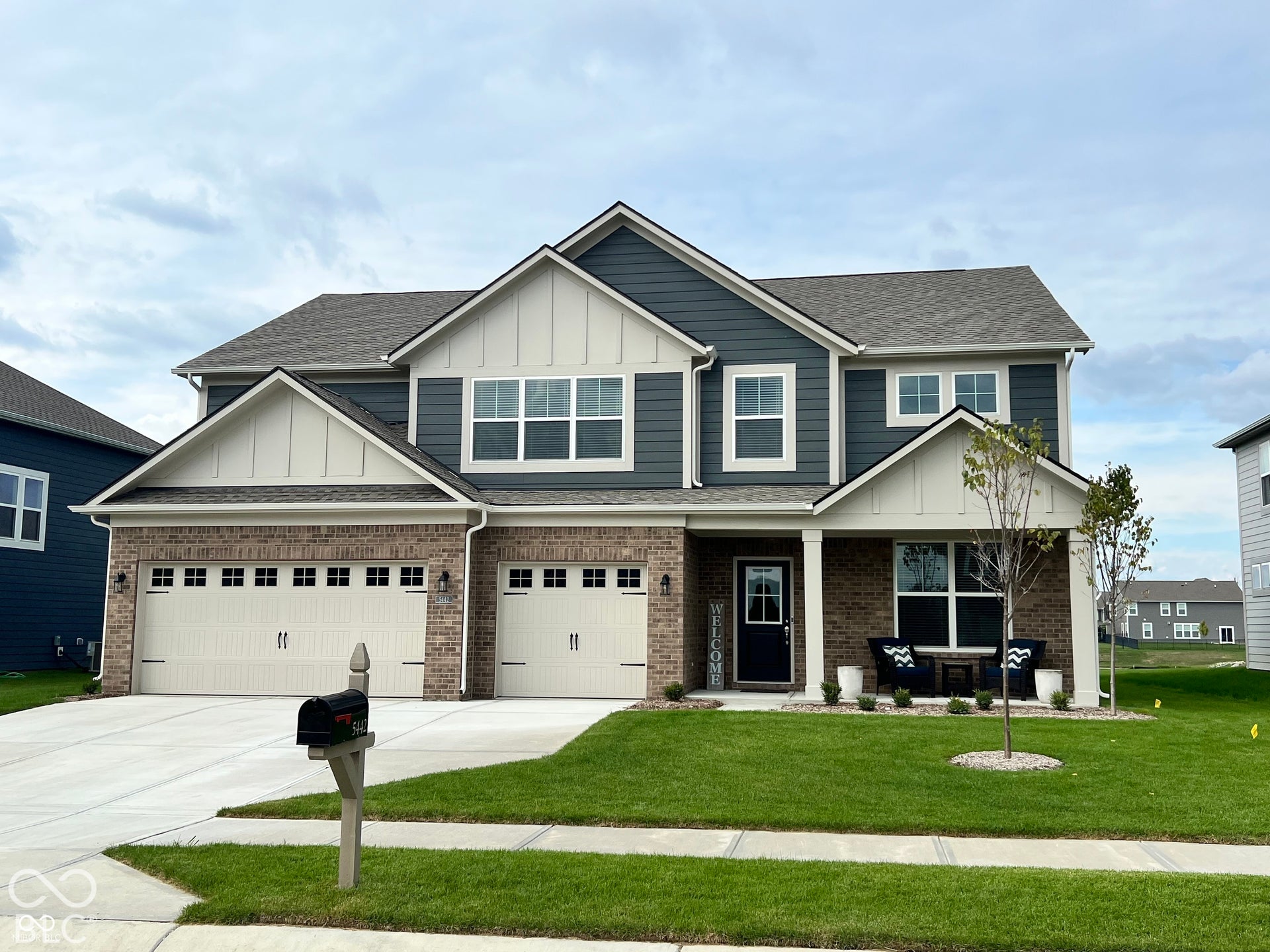 Multi-level exterior featuring a combination of brick and horizontal siding, a covered front porch with a support column, and a three-car garage with carriage-style doors