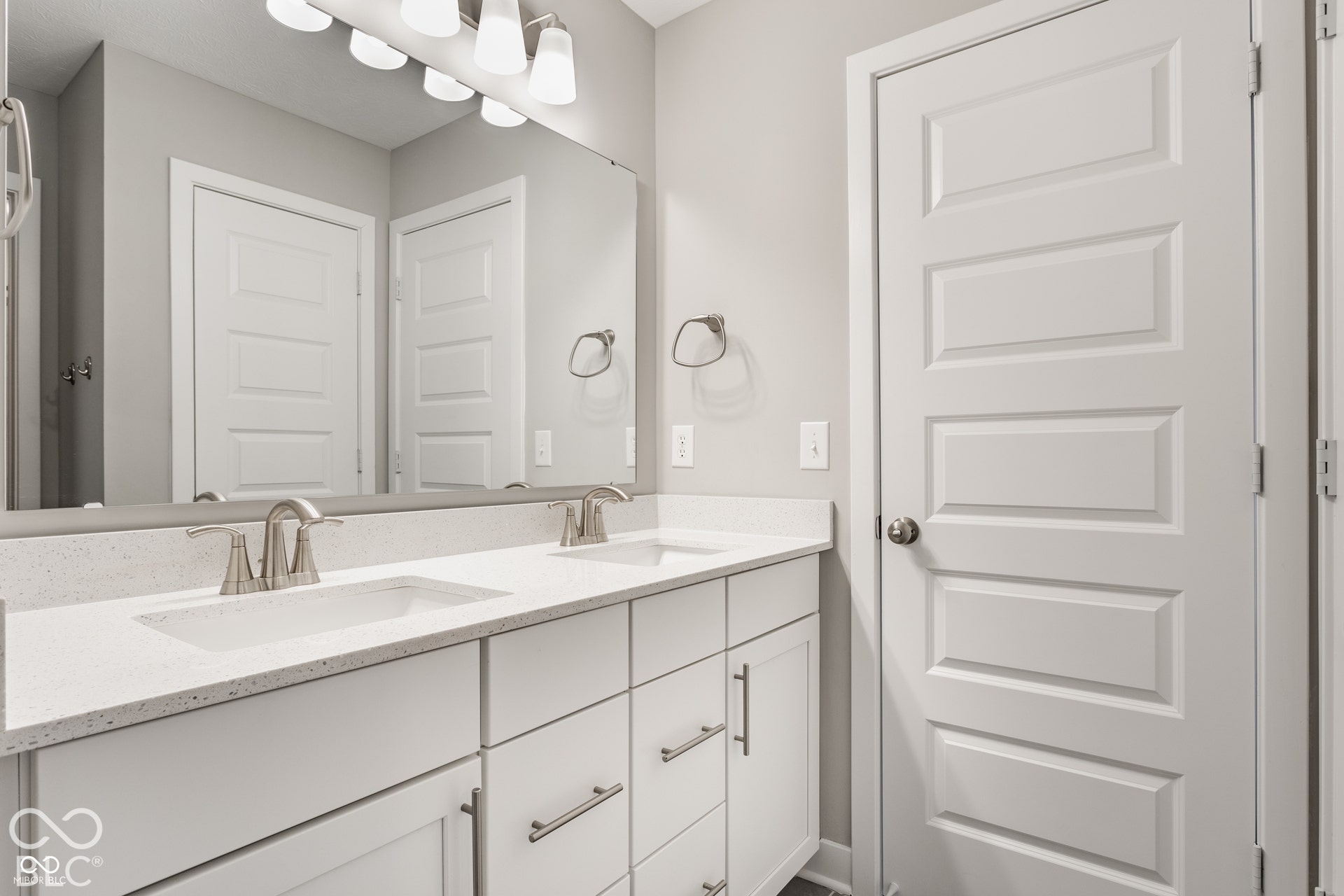 Double-sink vanity with quartz countertop, under-mount basins, brushed nickel hardware, expansive wall-mounted mirror, and five-panel interior door