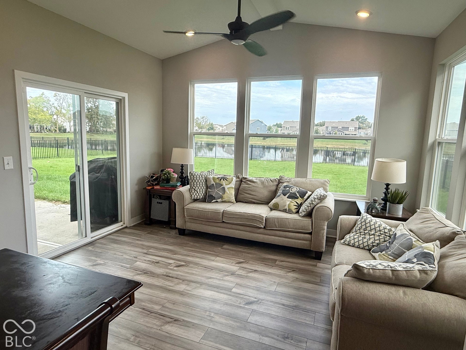 Vaulted ceilings with a ceiling fan, wood-finish flooring, and large windows featuring pond water frontage