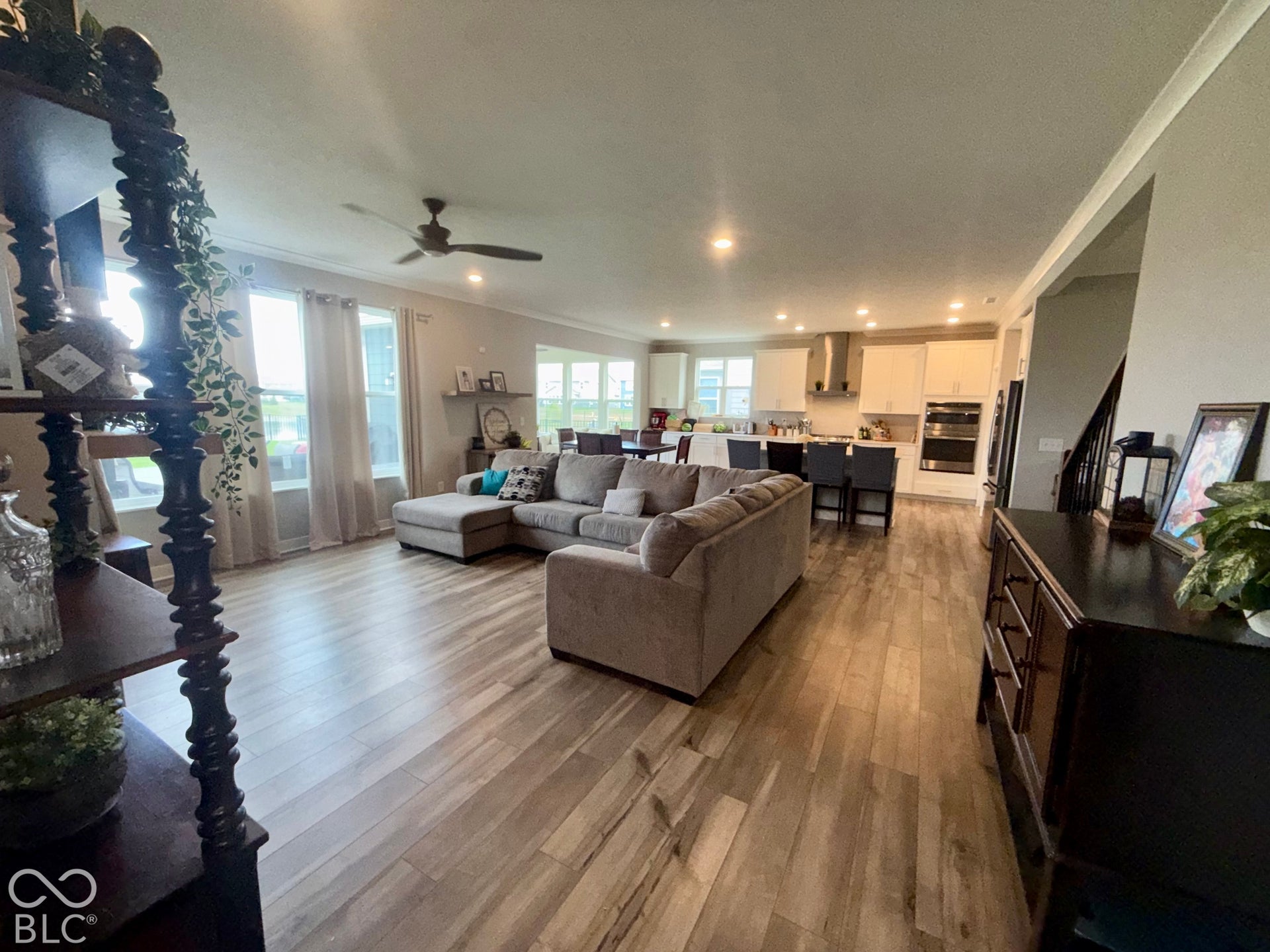 Open-concept interior featuring wood-finish flooring, recessed lighting, a ceiling fan, and a kitchen equipped with white cabinetry, a stainless steel range hood, and built-in wall ovens
