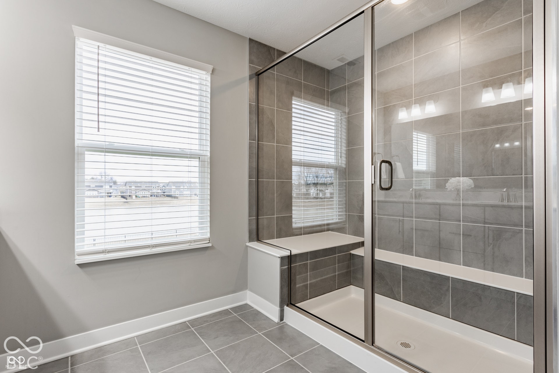 Walk-in shower featuring tile surrounds, a built-in bench seat, a glass enclosure with metallic framing, and tile flooring