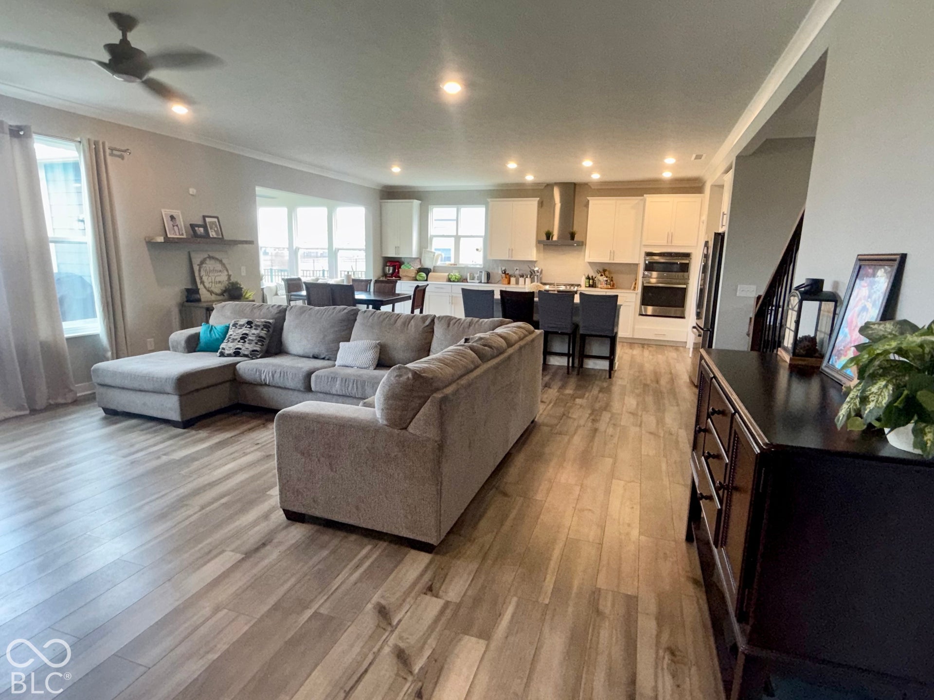 Open-concept interior featuring wood-finish flooring, recessed lighting, white cabinetry, a stainless steel range hood, and a built-in wall oven