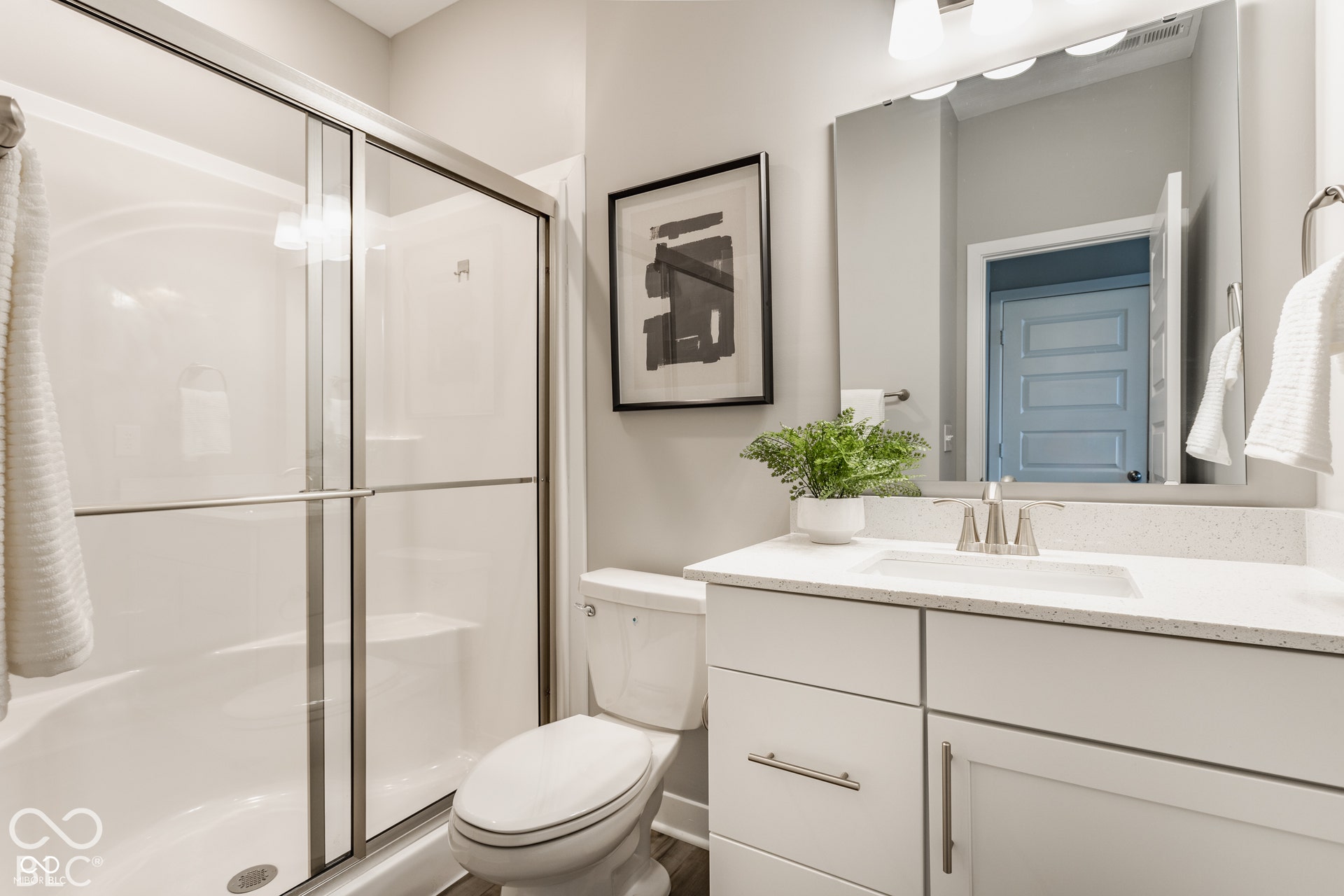 Bathroom featuring a white vanity with a composite countertop, undermount sink, brushed nickel faucet, large wall-mounted mirror, and a walk-in shower with a glass sliding door