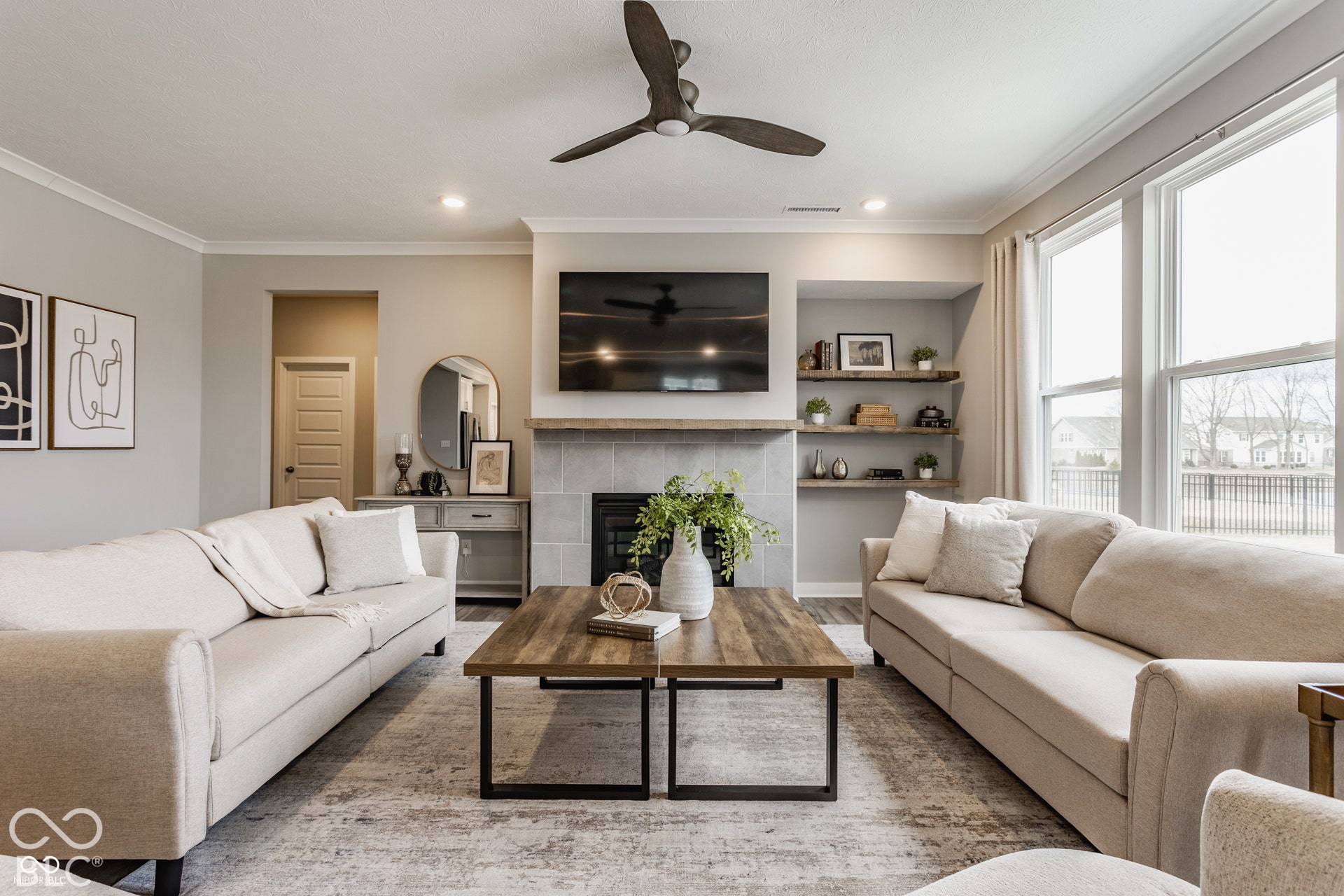 Fireplace featuring a large-format tile surround and wood mantel, built-in recessed shelving, oversized windows, crown molding, and a modern ceiling fan