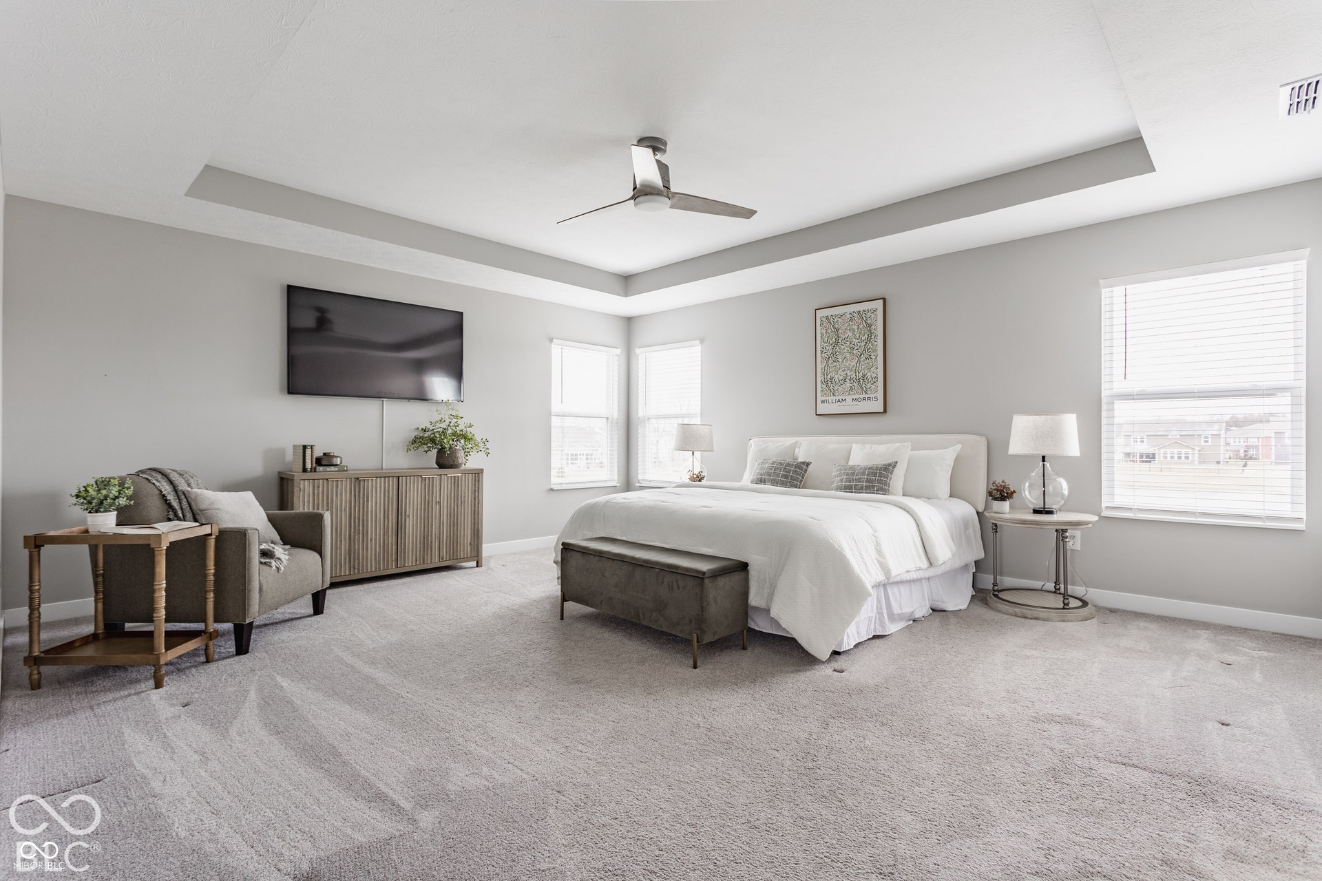 Spacious room featuring a tray ceiling, neutral wall tones, wall-to-wall carpeting, multiple windows with horizontal blinds, and a ceiling fan