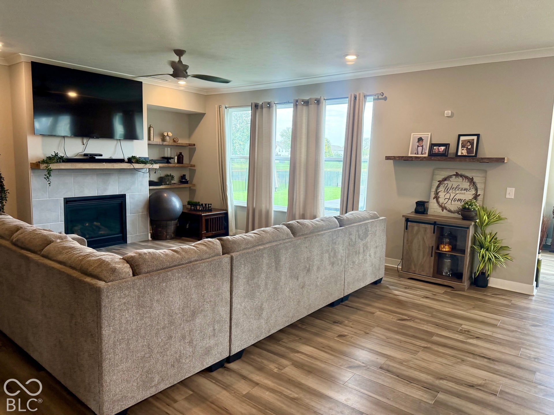 Living area featuring wood-finish flooring, a tile-surround fireplace, built-in recessed shelving, a natural wood floating mantel, and multiple large windows