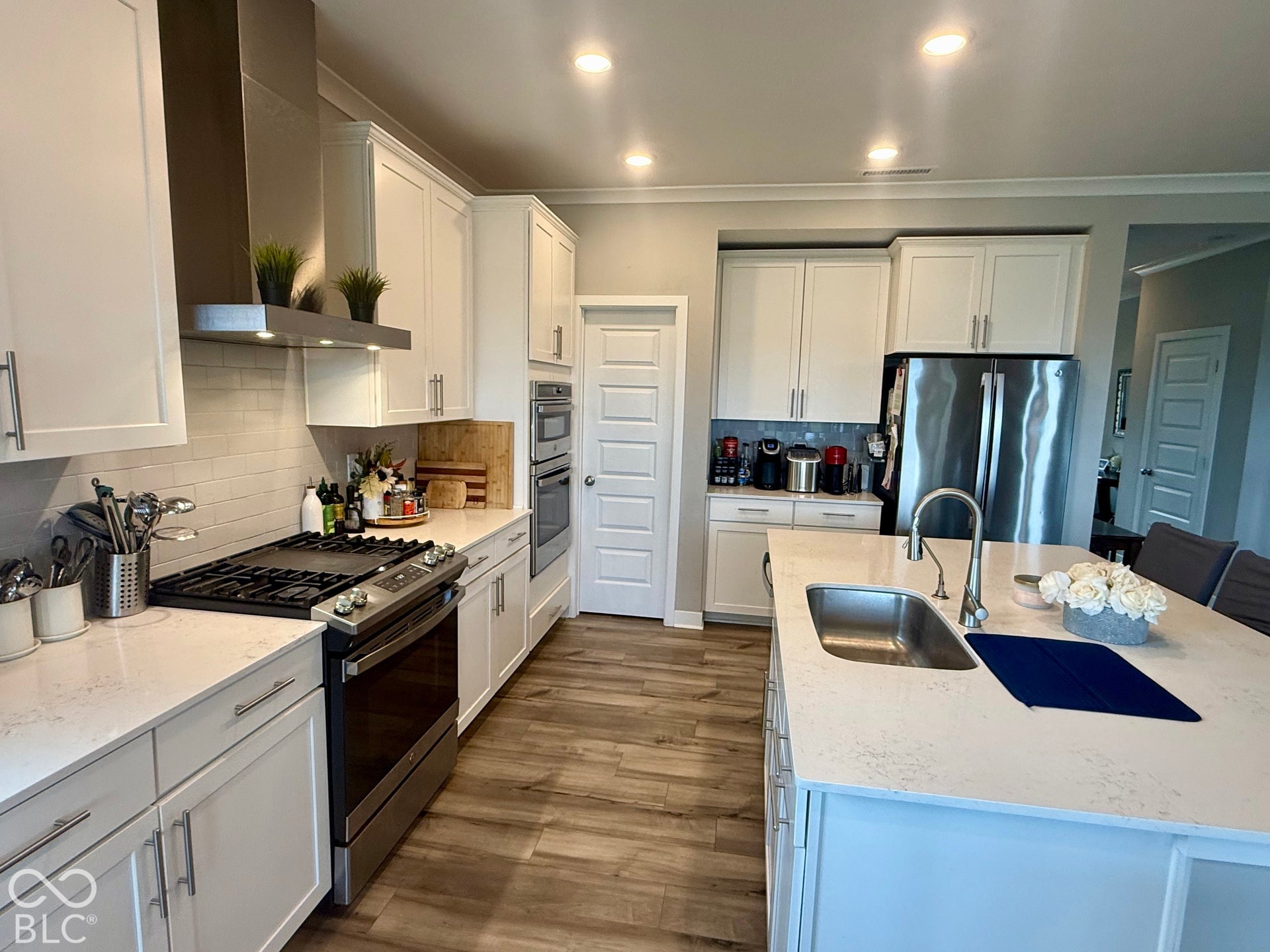 Kitchen featuring white cabinetry, quartz countertops, a central island with a stainless steel undermount sink, a stainless steel gas range with a matching range hood, and wood-finish flooring