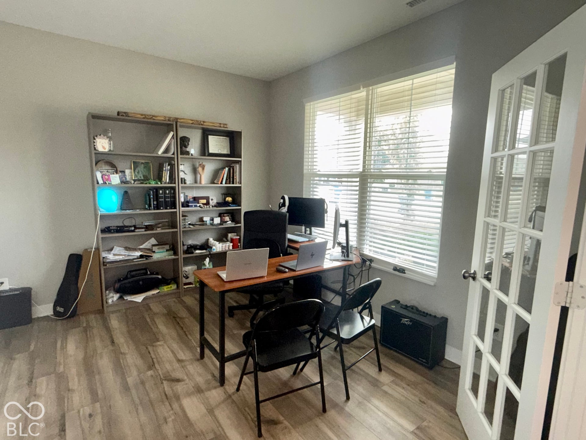 Neutral-toned room featuring wood-finish flooring, a large window with horizontal blinds, and a white-framed glass pane door