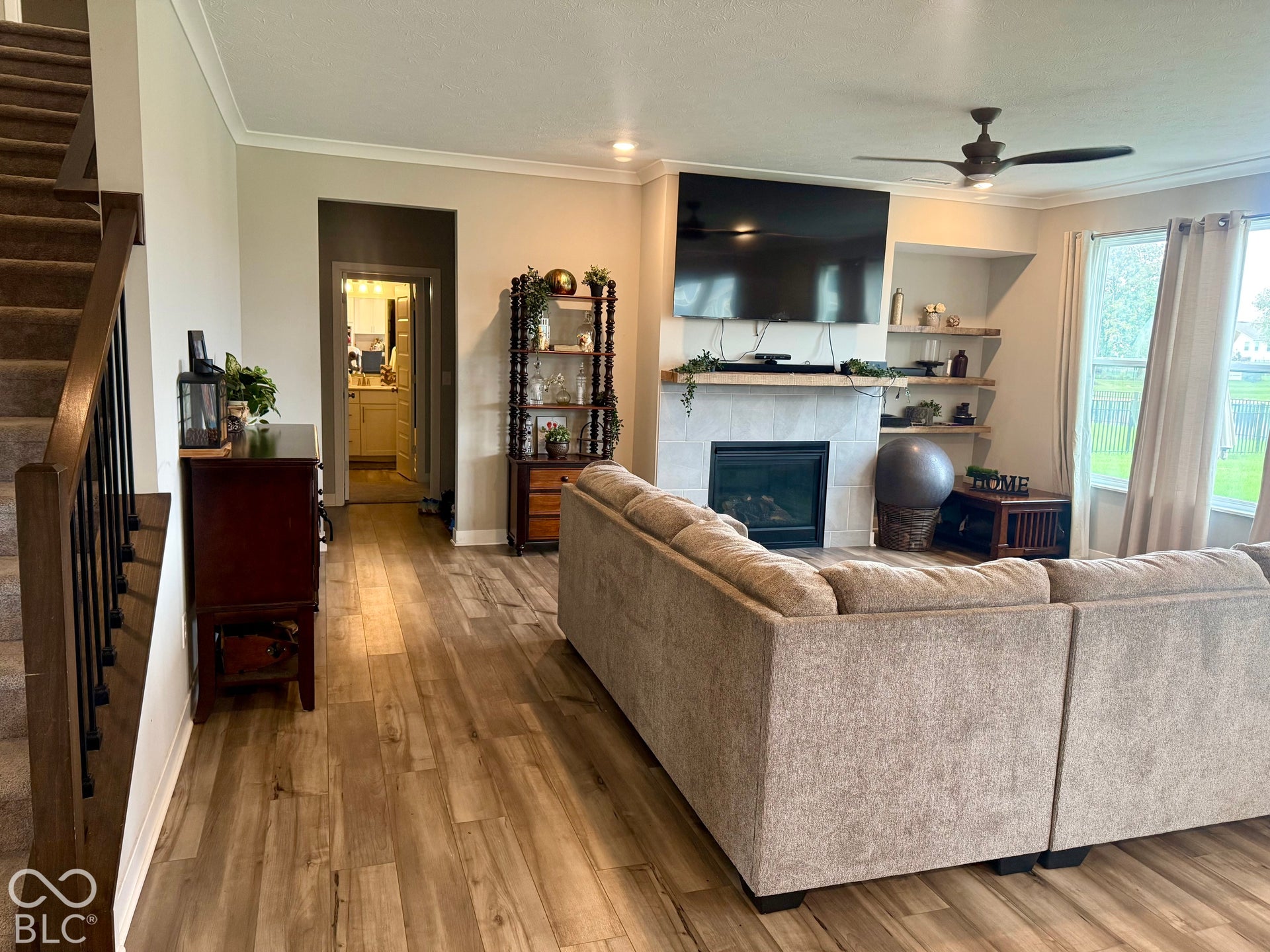 Living area featuring wood-finish flooring, a fireplace with a tile surround and wood mantel, built-in recessed shelving, and a ceiling fan