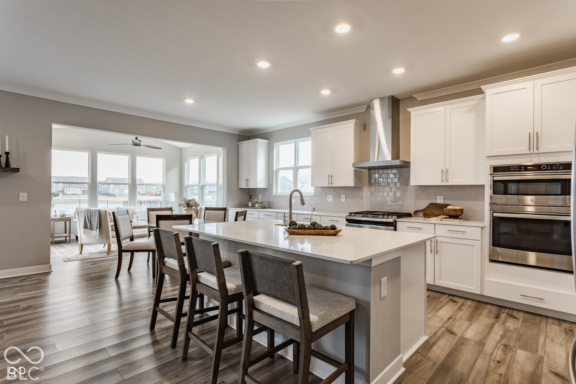 Kitchen featuring wood-finish flooring, white shaker-style cabinetry, quartz countertops, a stainless steel chimney-style range hood, and a built-in wall oven