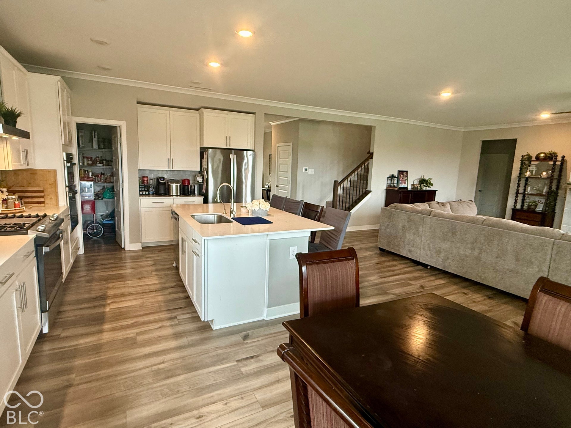 Kitchen featuring white cabinetry, quartz countertops, a central island with a stainless steel undermount sink, stainless steel appliances, and wood-finish flooring