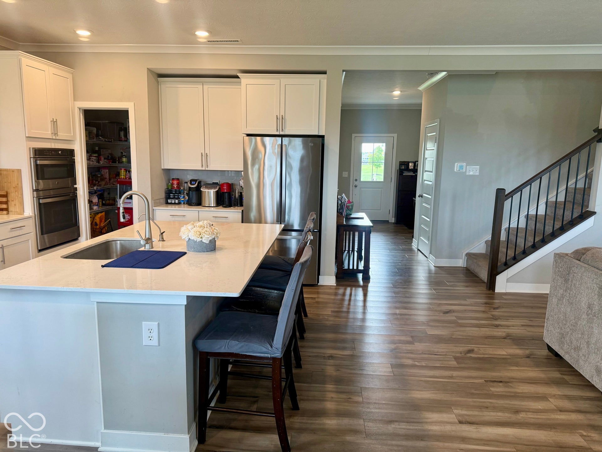 Kitchen featuring white shaker cabinetry, an expansive center island with a stone-composite countertop, stainless steel double wall ovens, a reach-in pantry, and wood-finish flooring