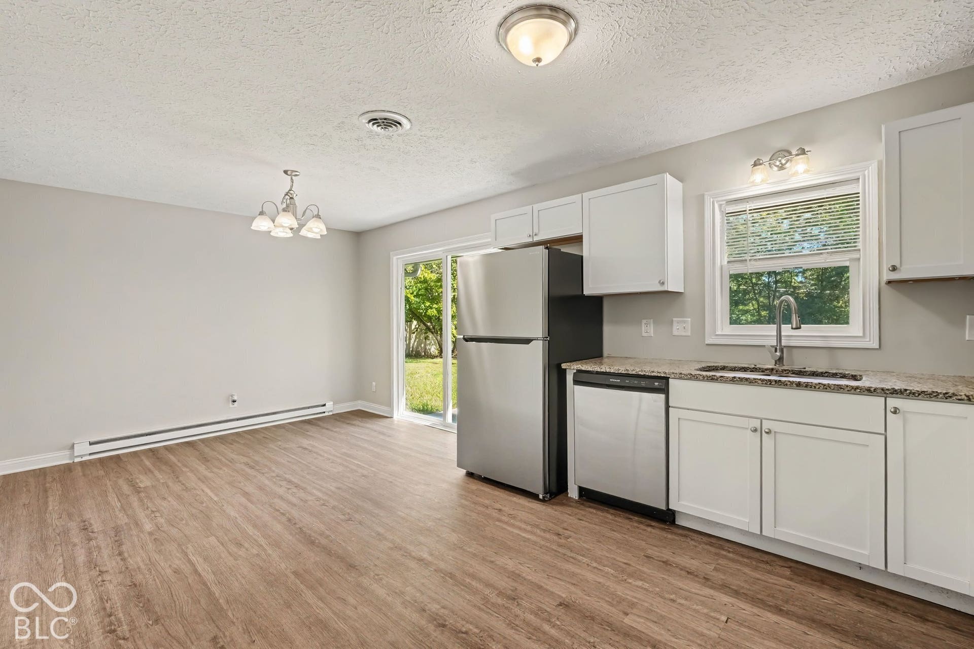 Wood-finish flooring throughout, white shaker-style cabinetry, stainless steel appliances, granite-look countertops, and a sliding glass door