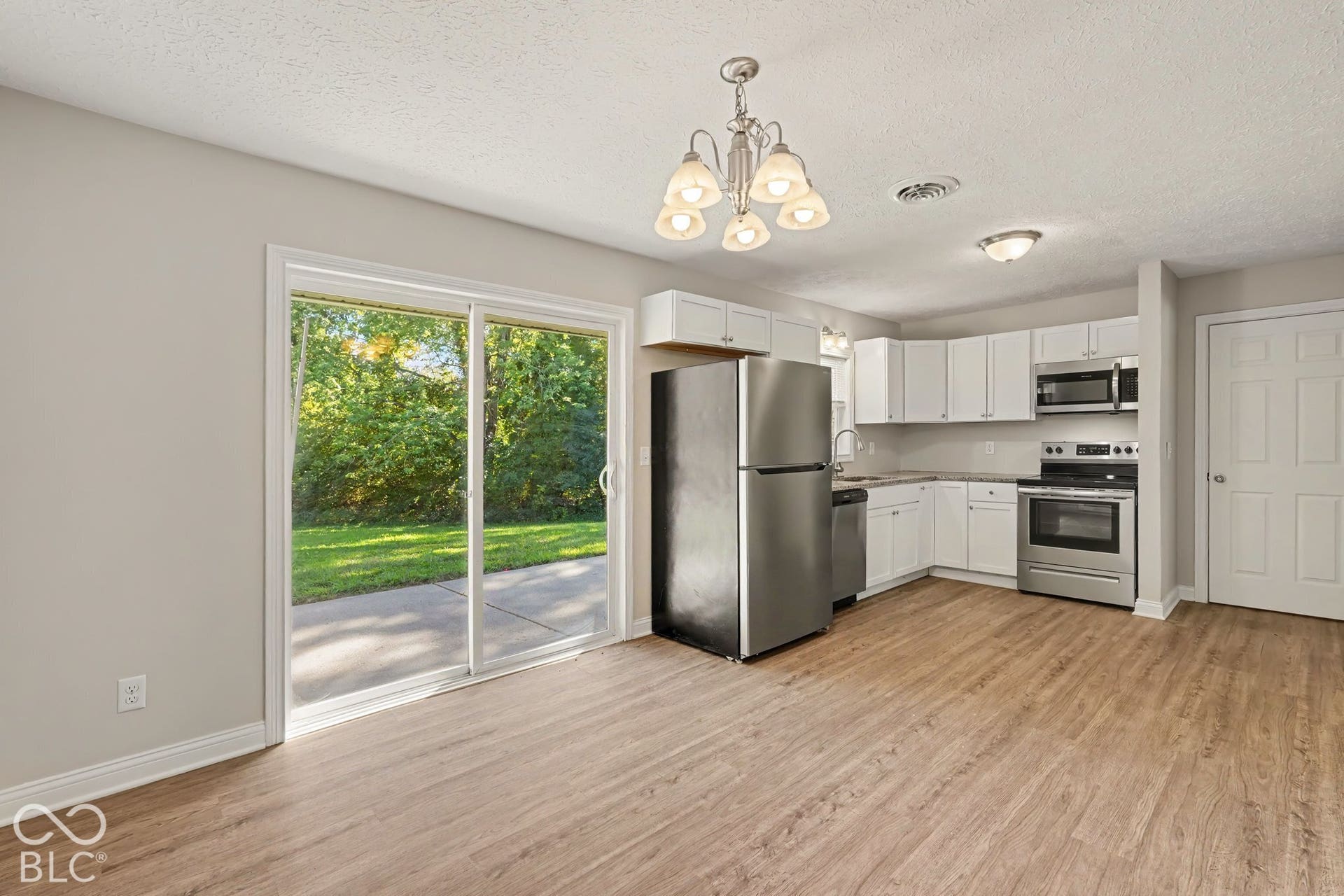 Kitchen featuring wood-finish flooring, white cabinetry, stainless steel appliances, and a sliding glass door to a patio