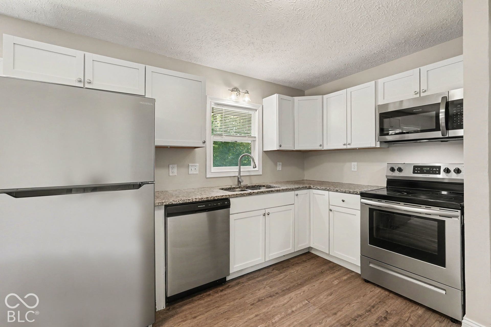 Kitchen featuring white cabinetry, wood-finish flooring, stainless steel appliances, granite-style countertops, and an undermount sink