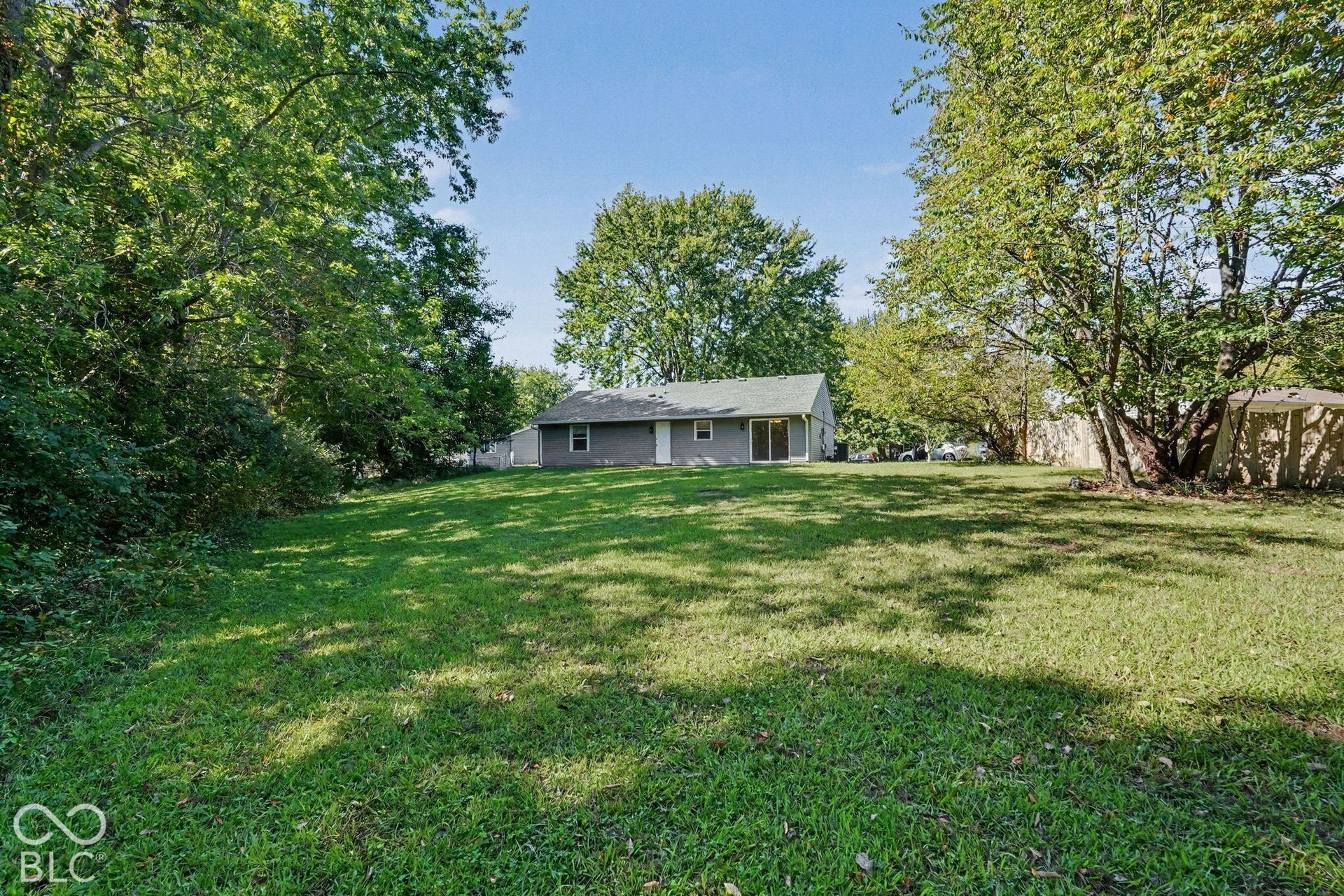 Expansive lawn framed by mature trees, featuring a detached single-story residence with gray siding and a light-colored roof