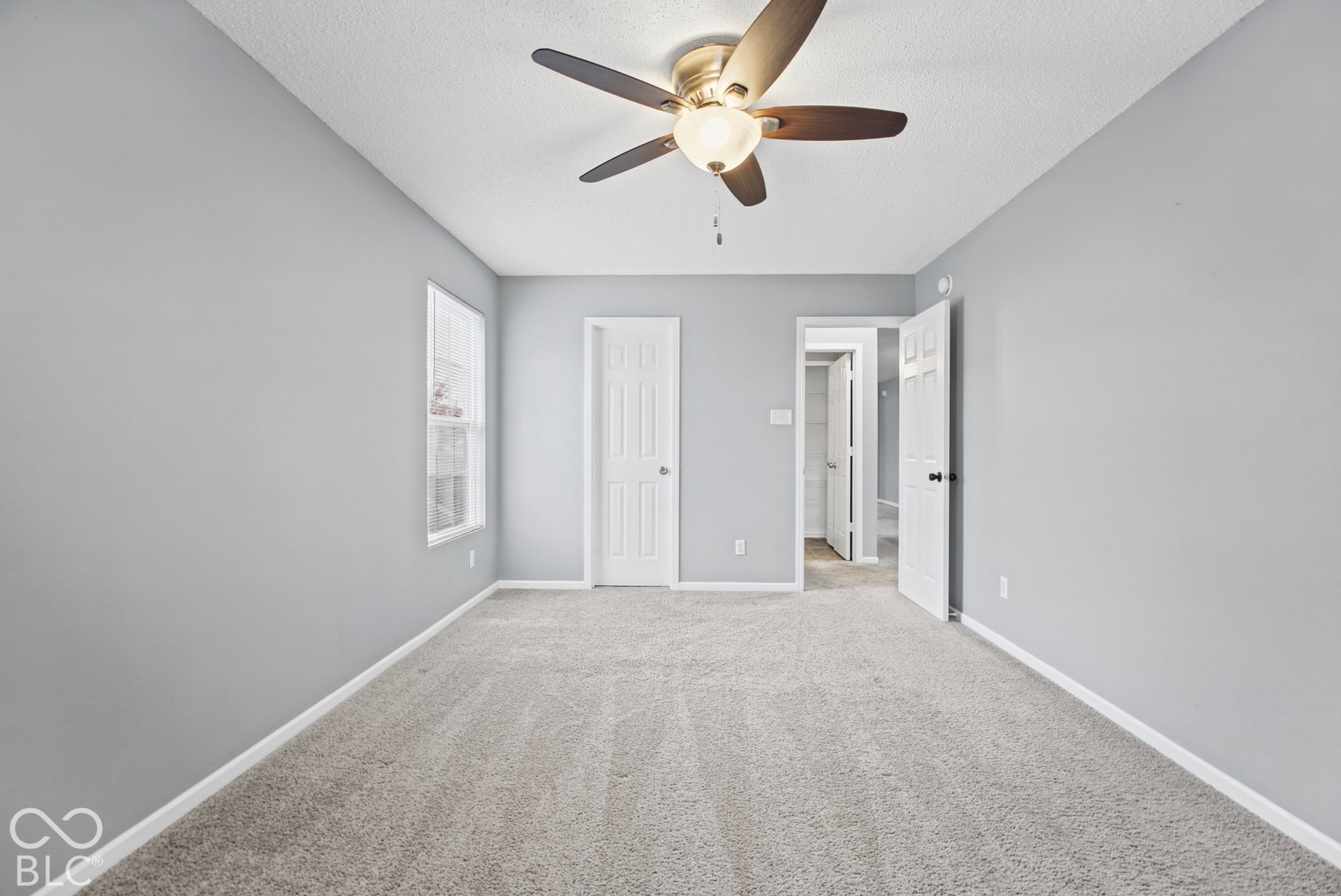 Neutral-toned walls, wall-to-wall carpeting, and a ceiling-mounted fan with integrated lighting