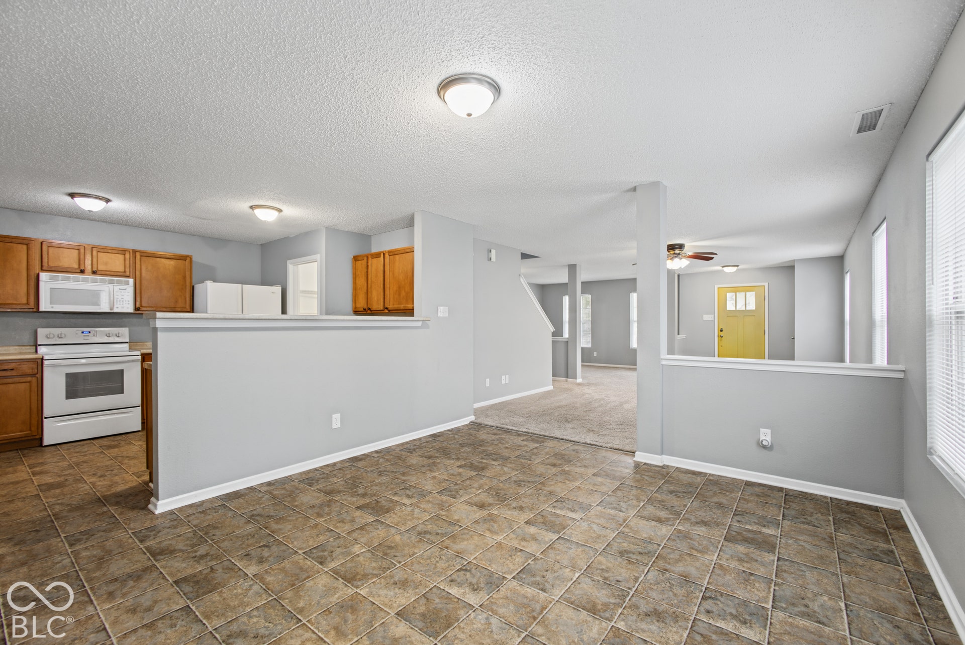 Open-concept interior featuring tile flooring, wood-finish cabinetry, white built-in appliances, and recessed ceiling lighting