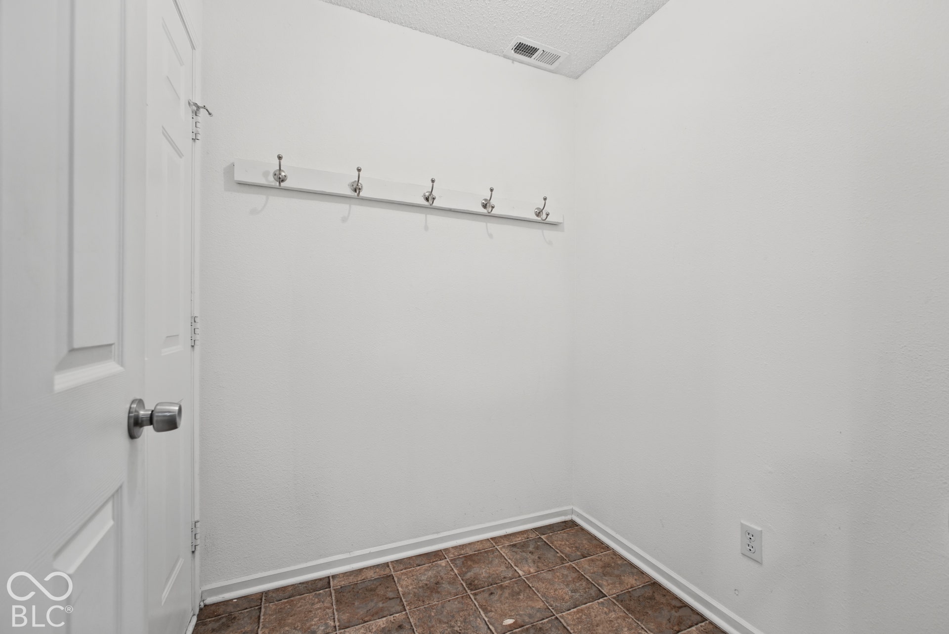 Interior area featuring tile flooring, a mounted horizontal coat rack with five hooks, and a paneled interior door with a brushed metallic handle